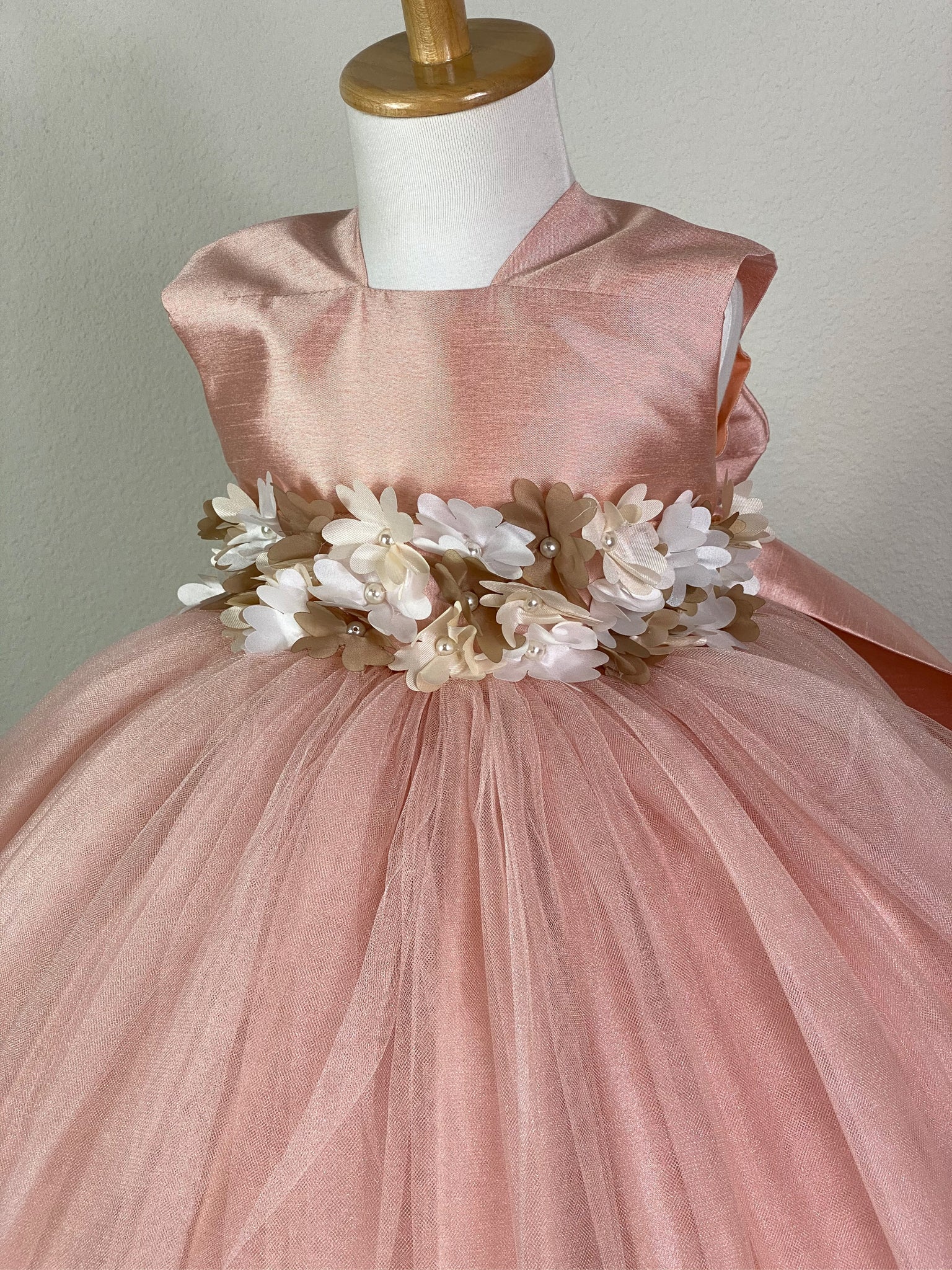 BLUSH  Blush squared neck bodice Ivory and beige flower with pearl center cummerbund Blush ruched tulle and satin skirting Button closure Large blush bow on back Dress pictured with a petticoat Petticoat not included  Choose from a tulle, cloth, or wire for best look