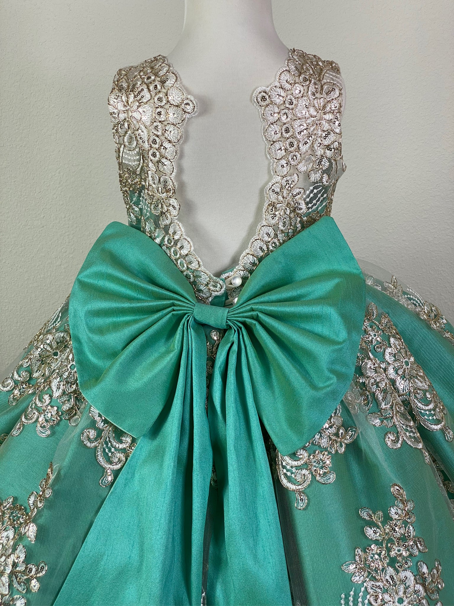 Menta Green, size 4 illusion bodice with embroidered white appliques on tulle Embellished rhinestone band along lower bodice Menta blue satin skirting with embroidered white appliques on tulle overlay Open back with button closure Large menta blue satin bow Dress pictured with a petticoat Petticoat not included  Choose from a tulle, cloth, or wire for best look