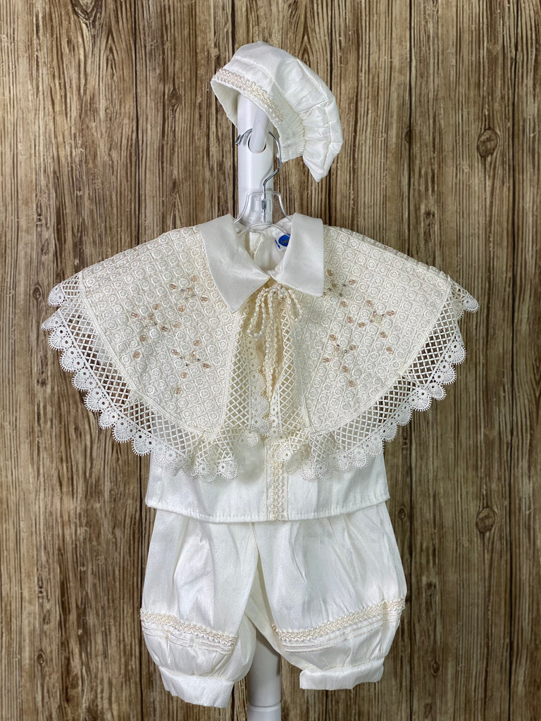 IVORY   4-piece ivory set including mozzetta, beret, shirt, suspender pants Collared romper with short sleeves Buttoning on pant cuffs Button closure on back of shirt Pin tucks overlapping diagonal with pin wheel detailing inside on mozzetta Wide embroidered lace trim around mozzetta Pearl and champagne jeweled crosses on mozzetta Rope closure on mozzetta Braided embroidered line detailing on pant, cummerbund, sleeves, beret, and down shirt center