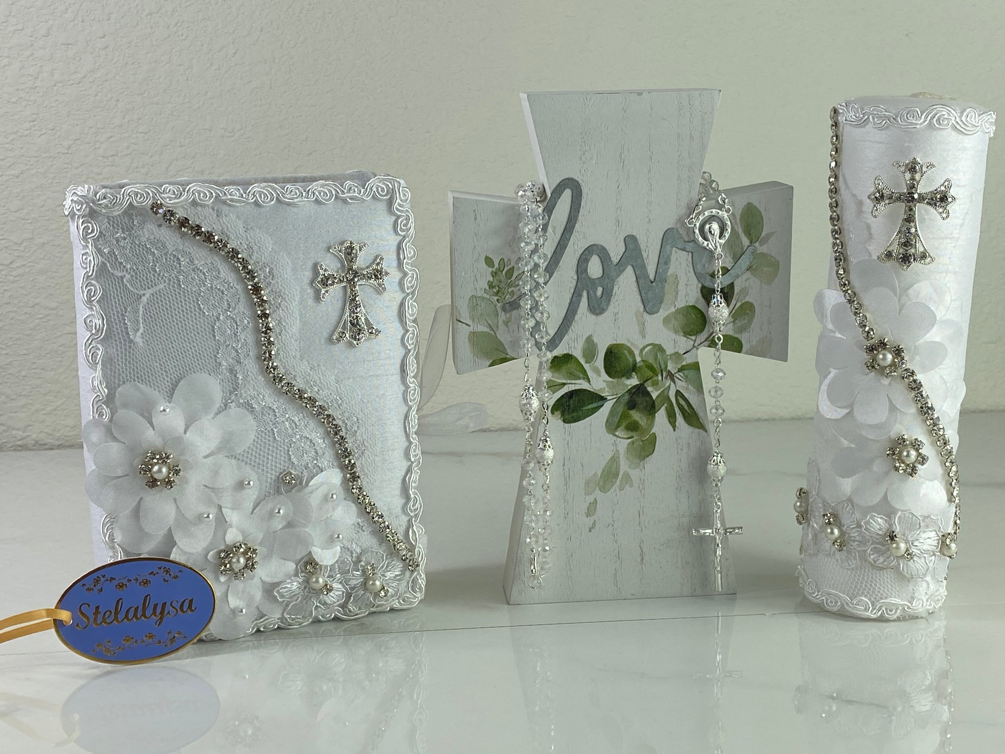 This ivory Bible Set - candle and bible is handmade and made using satin and lace.  It is elegantly designed with pearls, crystals, flowers and beads.  Each piece has a beautiful cross.   An elegant rosary complements this set.  The candle is cylinder in shape. The rosary is 16.5 in. long and Bible is 6.5 in. by 4.5 in. and the candles approximately the same height.  The Bible includes the Old and New Testament in English. 