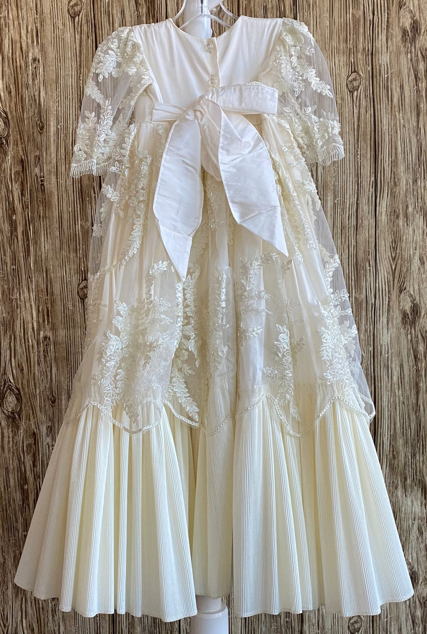 This a beautiful, one-of-a-kind baptism gown.  A lovely gown for a precious child.  Ivory, size 12M Embroidered beaded floral overlay on satin bodice Embroidered floral tulle half sleeve  Large rhinestone belt around bodice Long skirting with pleated ruffled bottom Embroidered beaded floral tulle overlay on skirt