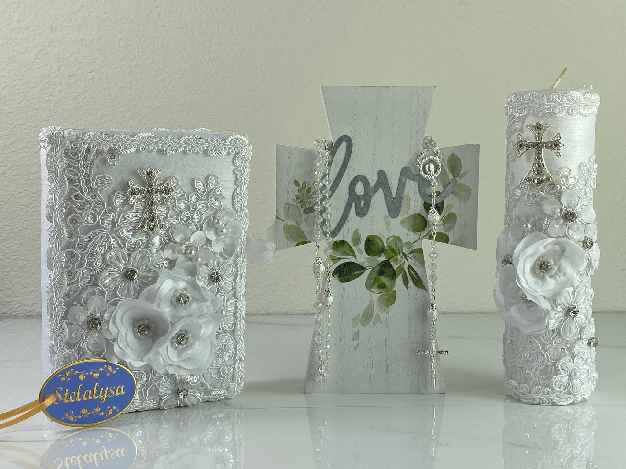 This white Bible Set - candle and bible is handmade and made using satin.  It is elegantly designed with lace, rhinestones, pearls, flowers, and sequins.  Each piece has a beautiful cross.  The candle is cylinder in shape.  An elegant rosary complements this set.  The rosary is 16.5 in. long and Bible is 6.5 in. by 4.5 in. and the candles approximately the same height.  The Bible includes the Old and New Testament in English. 