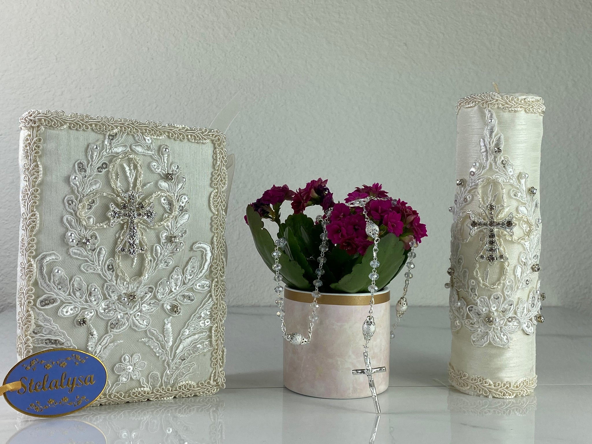 This ivory Bible Set - candle and bible is handmade and made using satin.  It is elegantly designed with lace, rhinestones, and pearls.  Each piece has a beautiful cross.  An elegant rosary complements this set.  The rosary is 16.5 in. long and Bible is 6.5 in. by 4.5 in. and the candles approximately the same height.  The Bible includes the Old and New Testament in English. 
