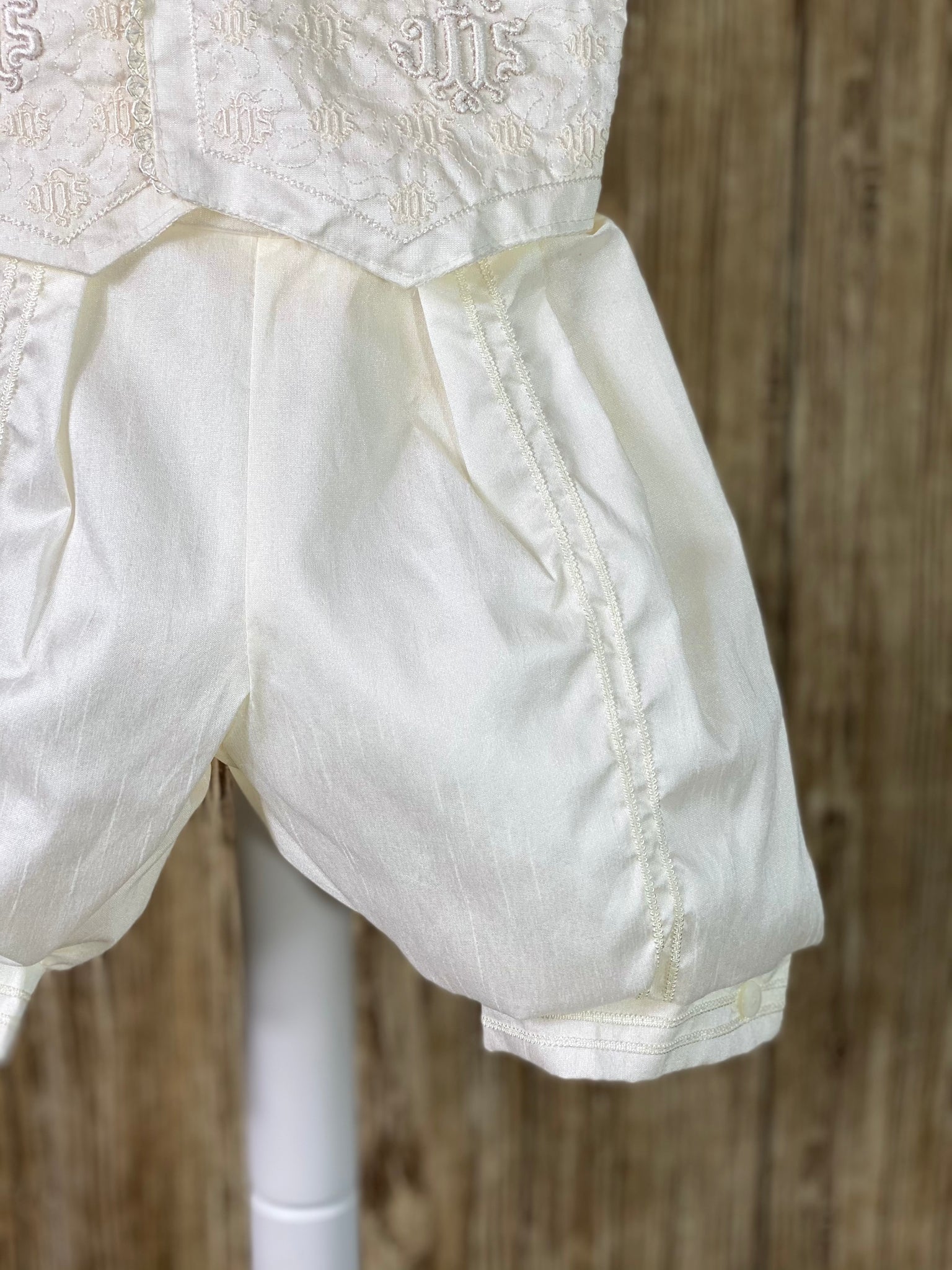 This a beautiful, one-of-a-kind boy’s baptism gown/set.  Lovely clothes for a precious child.   IVORY   4-piece white set including beret, vest, shirt, suspender pants JHS symbol embroidered into vest (JHS stands for Jesus Holmium Salvatore, Latin for Jesus Savior of Mankind) Tassel pin with 3 rhinestone centered circles Thin trim along cuffs, beret, and up pant legs Collared shirt with short sleeves Buttoning on pant cuffs Elastic banding behind pants Button closure on back of shirt