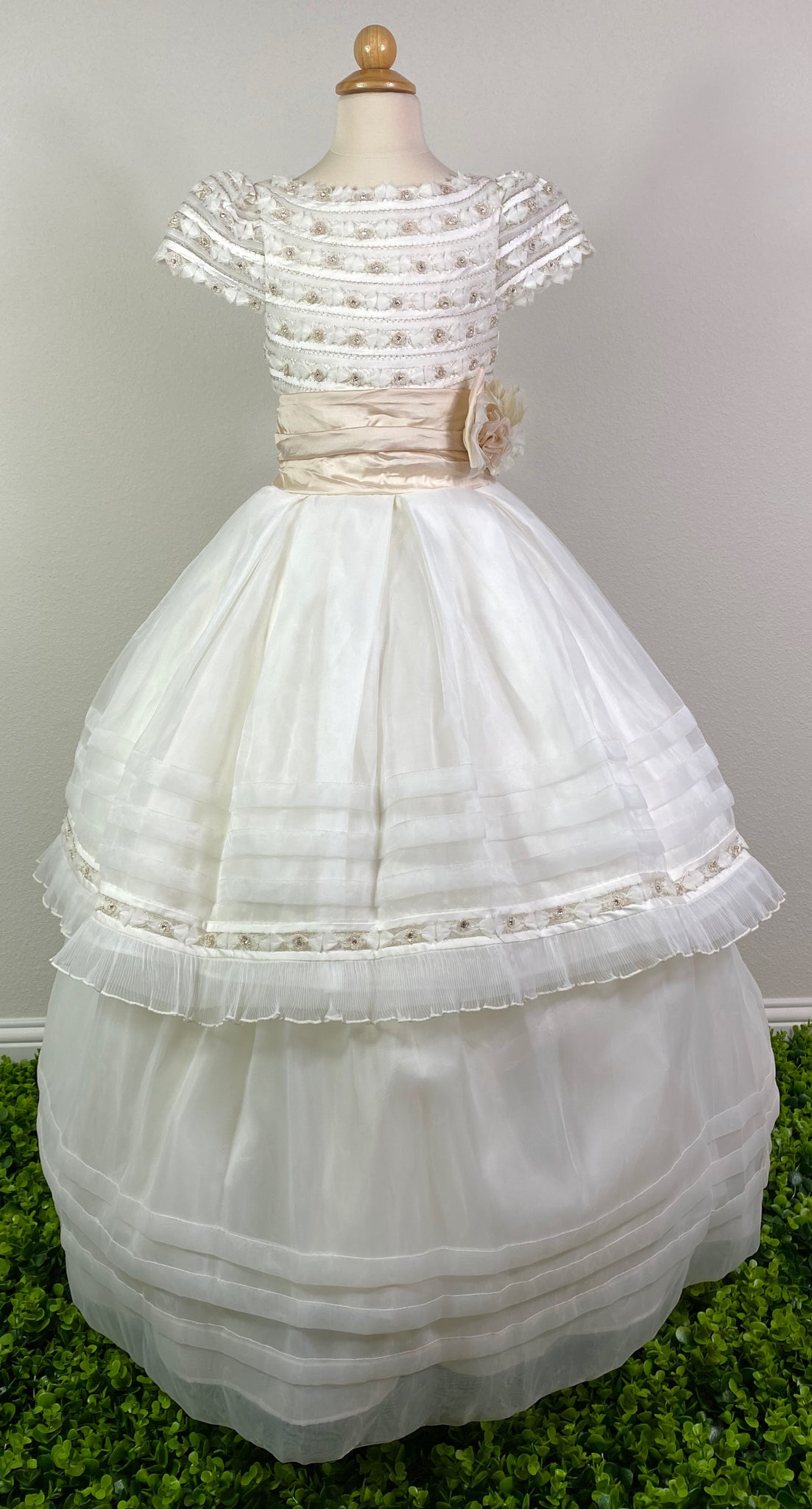 Ivory, size 12 Hand-stitched columned satin and flower bodice with crystals Extended scoop neckline Champagne cummerbund with ruffled bow Ivory tulle skirt with pleated trim and stripes along bottom Detachable skirt for long dress or short dress Satin covered button closure Champagne satin ribbon for large bow