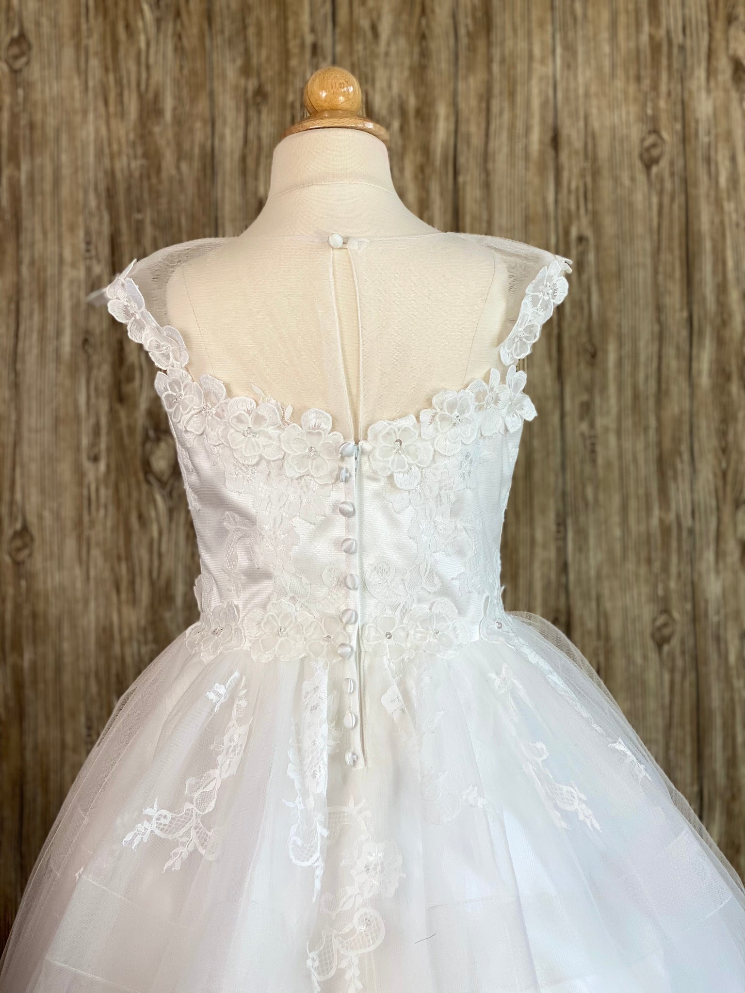 White, size 10 Lace illusion bodice with floral trim Layered tulle skirt with embroidered lace flowers Zipper closure with buttons over top