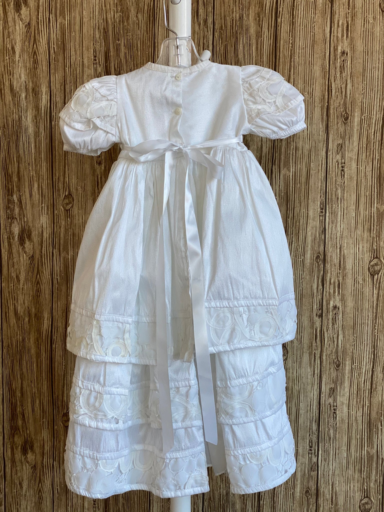 This a beautiful, one-of-a-kind baptism gown.  A lovely gown for a precious child.  White, size 12M Satin bodice Lace detailing along bodice and sleeves Rhinestones along bodice  Puffed sleeves Large flower  Satin skirting with lace detailing on edges  Select a beautiful headband to complete the outfit.  We have many to choose from.