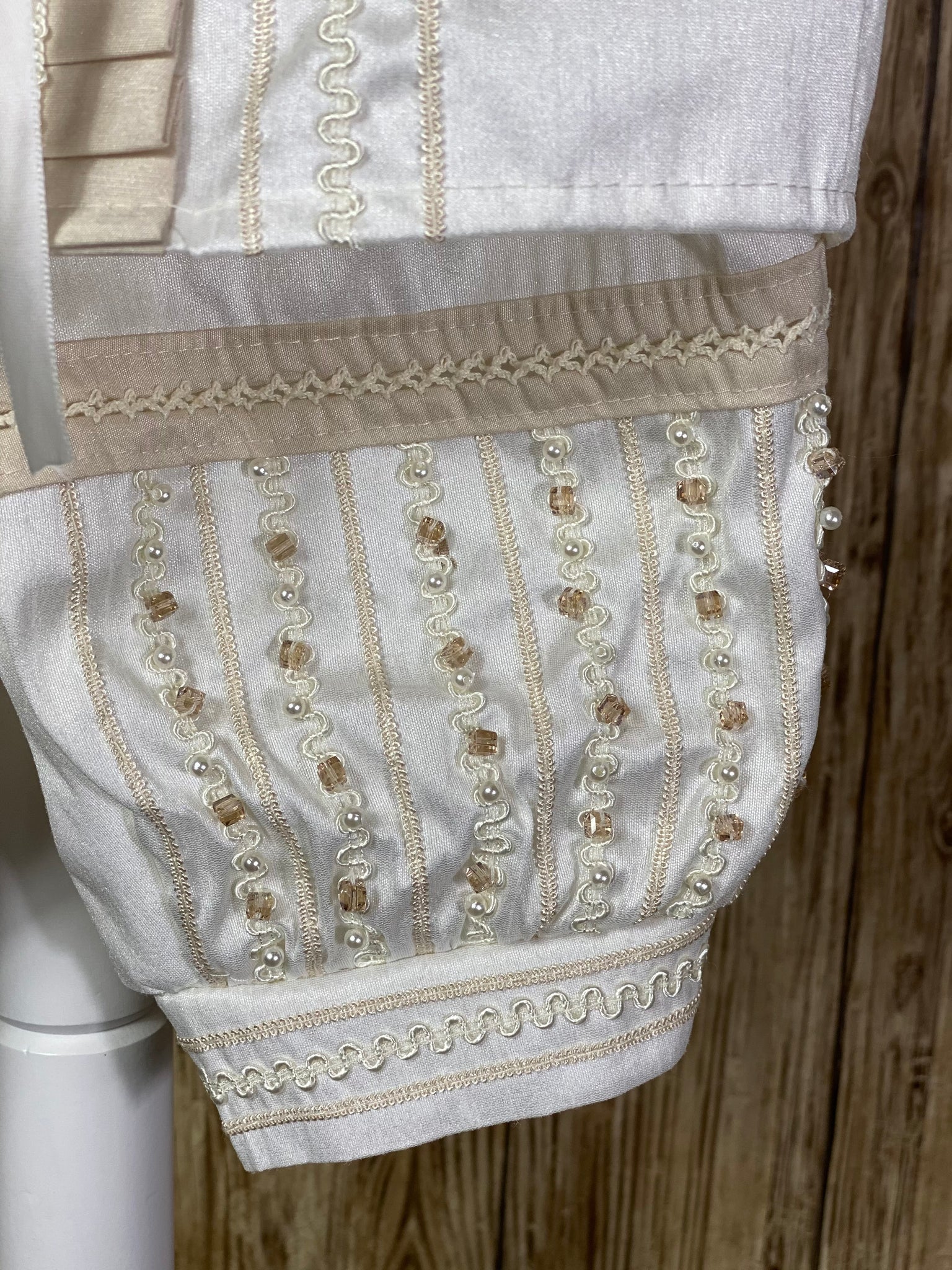 Ivory, size 6M  4-piece set including beret, mozzetta, shirt, suspender pants Vertical embroidery covering mozzetta, cummerbund, and pant legs Pearls and champagne jewels throughout embroidery Beige trim along mozzetta edge Intricate embroidered trim along mozzetta edge Ribbon closure on mozzetta Pleated beige detailing down center of shirt with rhinestone and pearl jewels Horizontal champagne rope detailing on pant cuffs Vertical champagne rope detailing on shirt center and beret