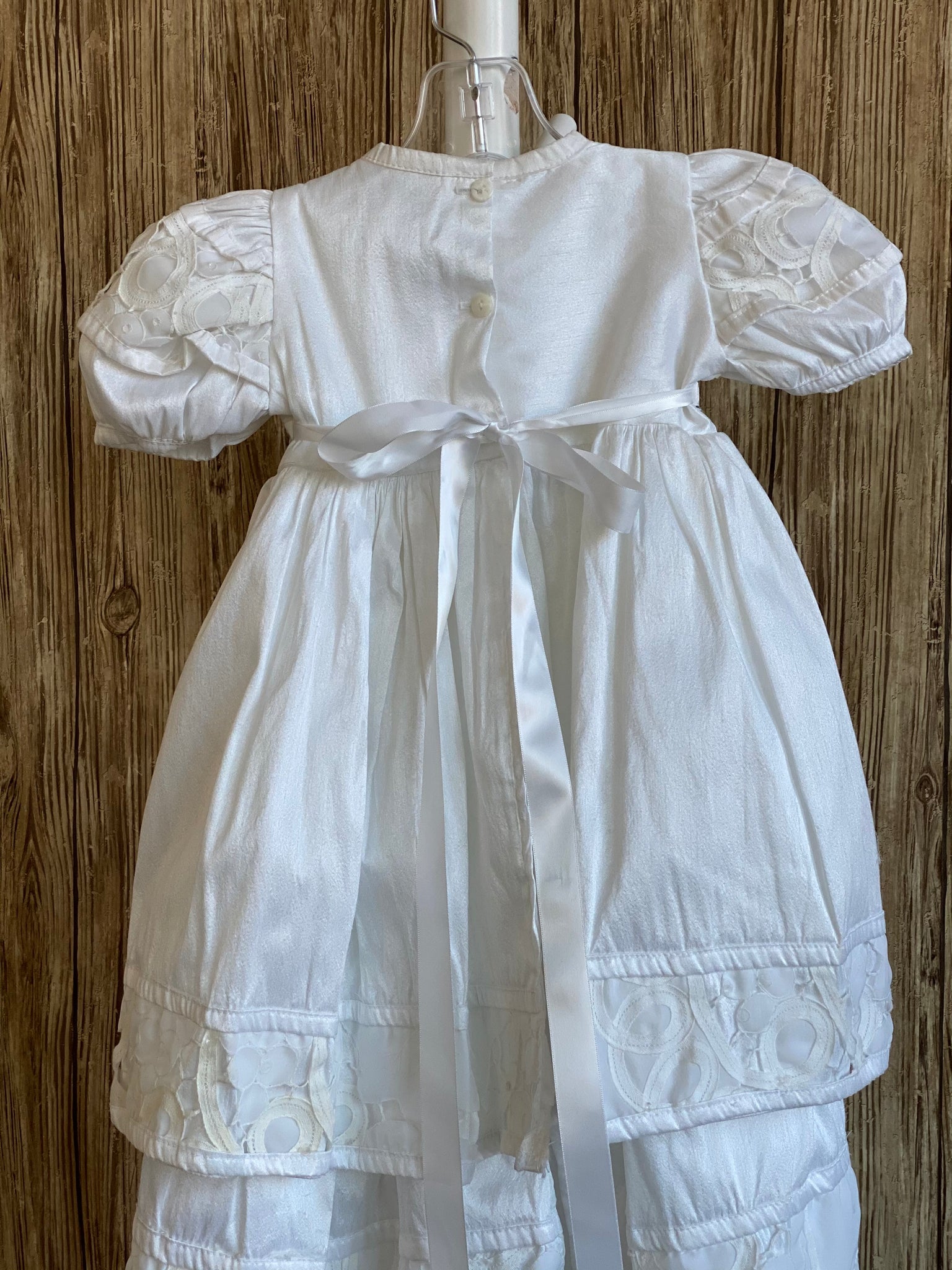 This a beautiful, one-of-a-kind baptism gown.  A lovely gown for a precious child.  White, size 12M Satin bodice Lace detailing along bodice and sleeves Rhinestones along bodice  Puffed sleeves Large flower  Satin skirting with lace detailing on edges  Select a beautiful headband to complete the outfit.  We have many to choose from.
