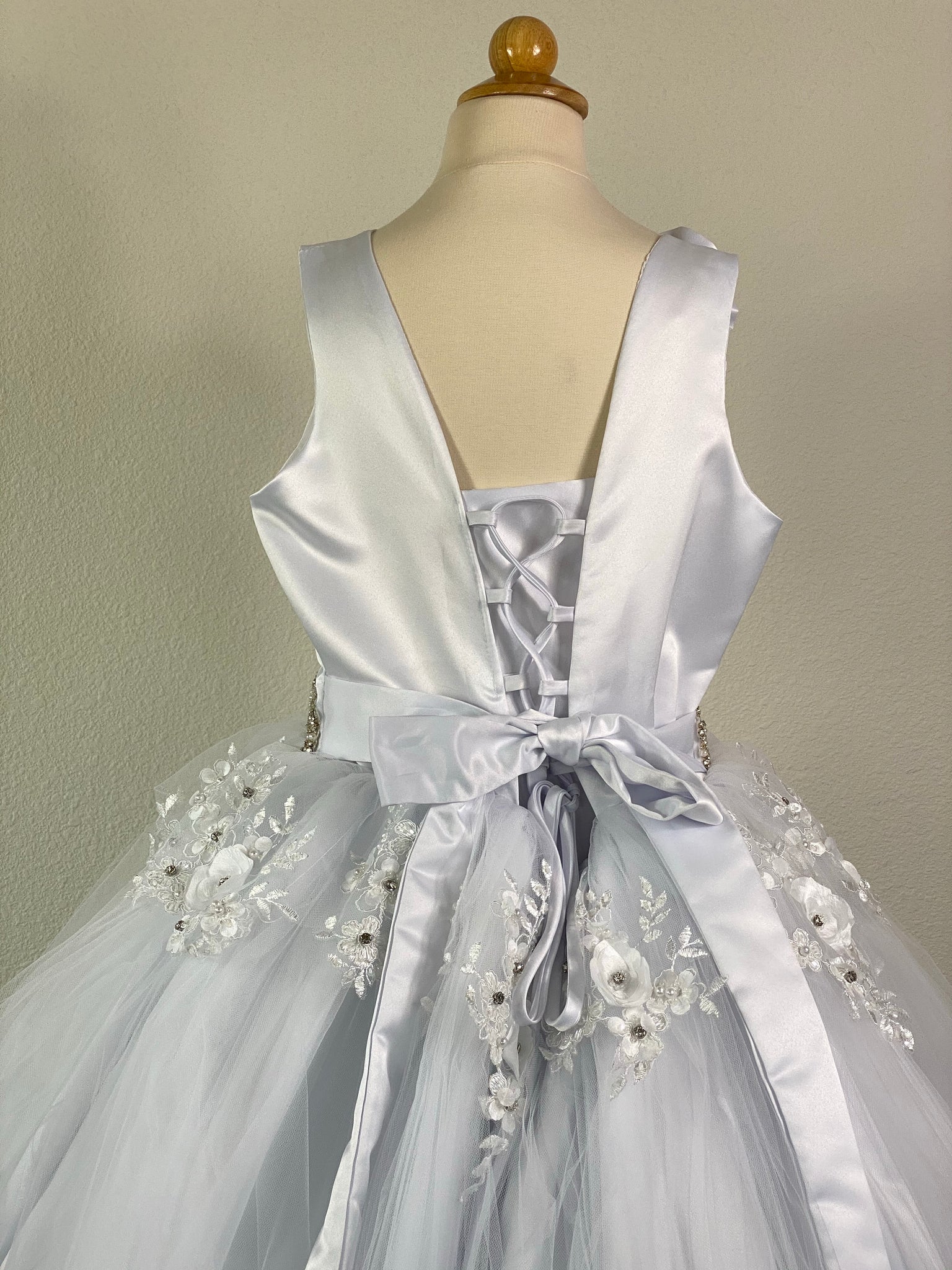 White, size 10 Satin bodice with flower on shoulder and embroidered lace detailing Pearl and rhinestone belt Layered tulle skirt with embroidered flowers with rhinestones on top layer Corset closure Satin ribbon for belt