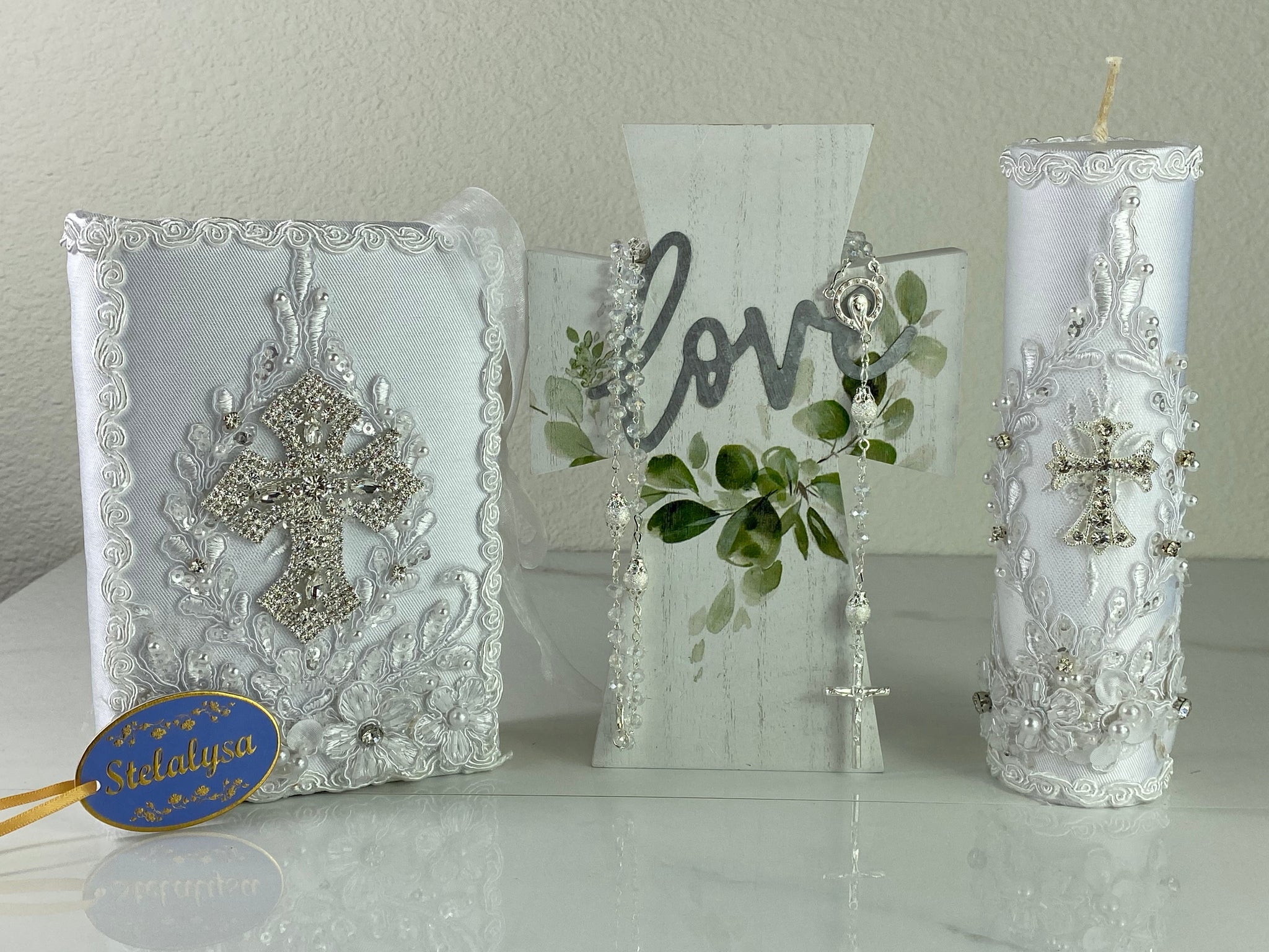 This white Bible Set - candle and bible is handmade and made using satin.  It is elegantly designed with lace, rhinestones, and pearls.  Each piece has a beautiful cross.  The candle is cylinder in shape.  An elegant rosary complements this set.  The rosary is 16.5 in. long and Bible is 6.5 in. by 4.5 in. and the candles approximately the same height.  The Bible includes the Old and New Testament in English. 