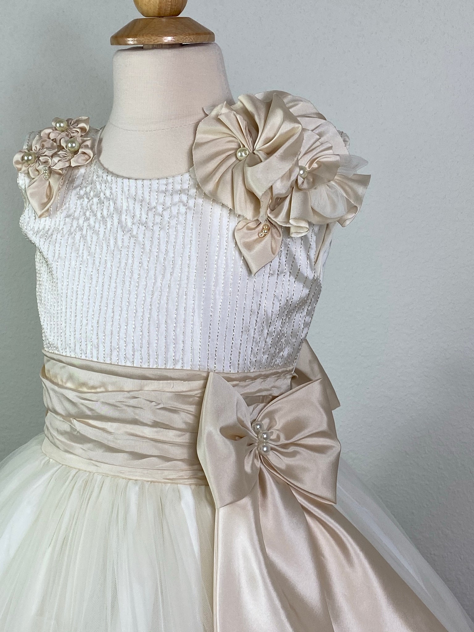 Ivory, size 8 Embroidered ivory pinstripe bodice with large pearled beige flowers on shoulder Beige cummerbund with pearl detailing on large bow Layered ivory tulle skirt with flower detailing on trim of first layer Six stacked braided stripes along edge of second tulle layer Satin covered button closure Beige Satin Ribbon for large bow