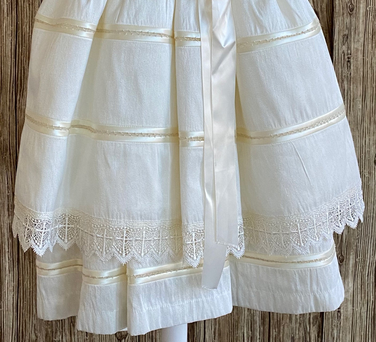 This a beautiful, one-of-a-kind baptism gown.  A lovely gown for a precious child.  Ivory, size 12M Satin bodice with hand embroidered floral design Handstitched layered cap sleeve Layered satin skirting with hemstitching between each layer Embroidered lace band around bottom layer  Long satin ribbon for bow