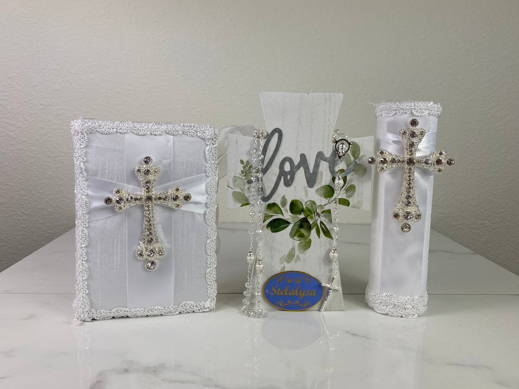 This white bible set is made with satin with a large cross elegantly decorated in rhinestones and lace trim for a classic look.  The candle's shape is a rectangular prism.  The rosary is 16.5 in. long and Bible is 6.5 in. by 4.5 in. and the candles approximately the same height.  The Bible includes the Old and New Testament in English. 