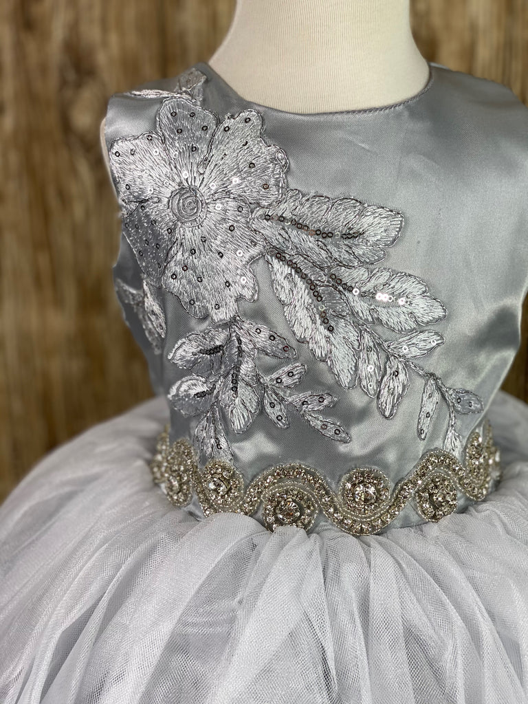 Silver, size 2 Silver bodice with large embroidered sequins and beaded flower on right side Swirled rhinestone band along lower bodice Silver satin and tulle skirting Button closure Silver ribbon for bow on back Dress pictured with a petticoat Petticoat not included  Choose from a tulle, cloth, or wire for best look