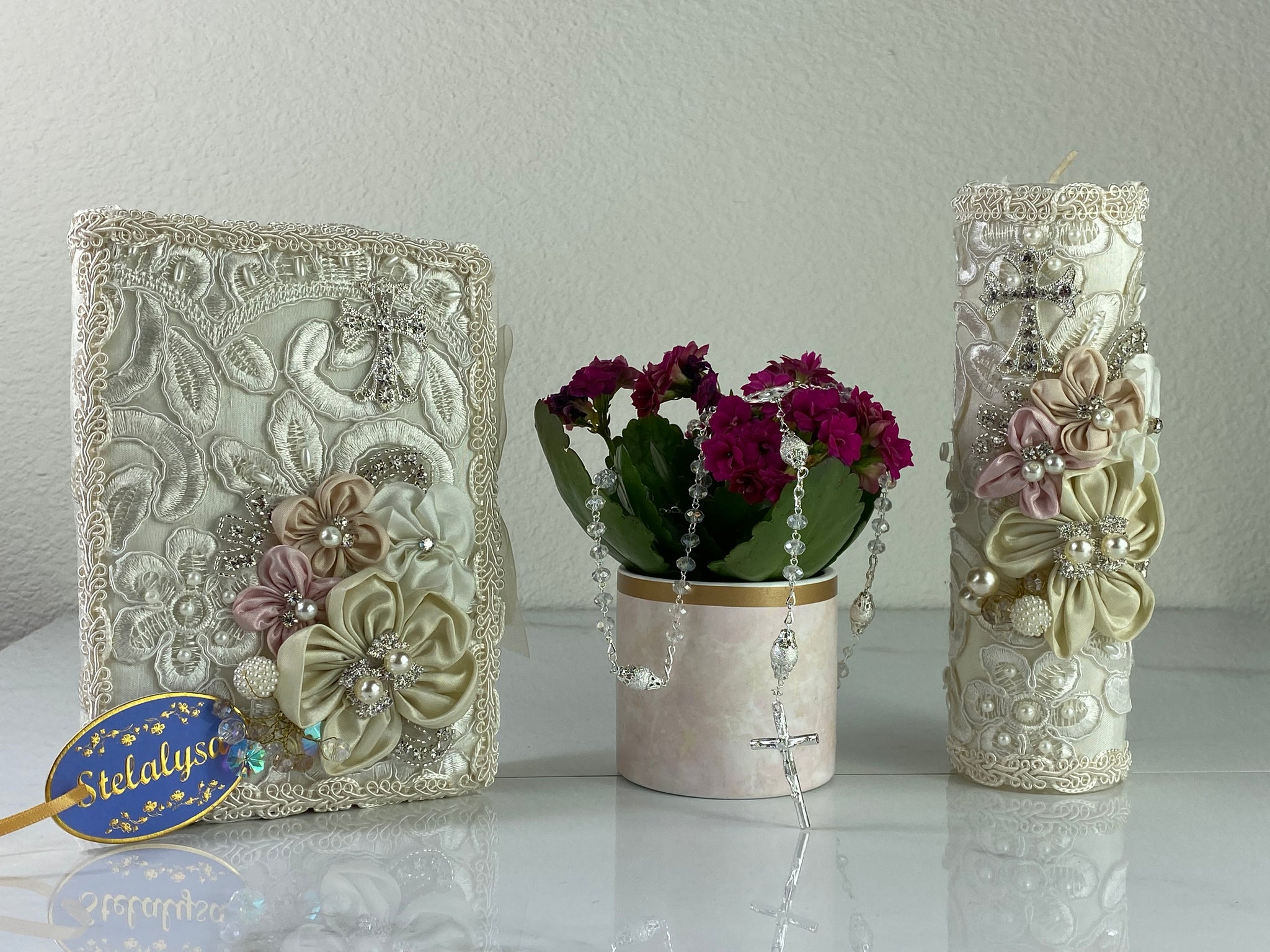 This ivory Bible Set - candle and bible is handmade and made using satin and lace.  It is elegantly designed with pearls, crystals, flowers in different pastel colors, and beads.  Each piece has a beautiful cross.  An elegant rosary complements this set.  The rosary is 16.5 in. long and Bible is 6.5 in. by 4.5 in. and the candles approximately the same height.  The Bible includes the Old and New Testament in English. 