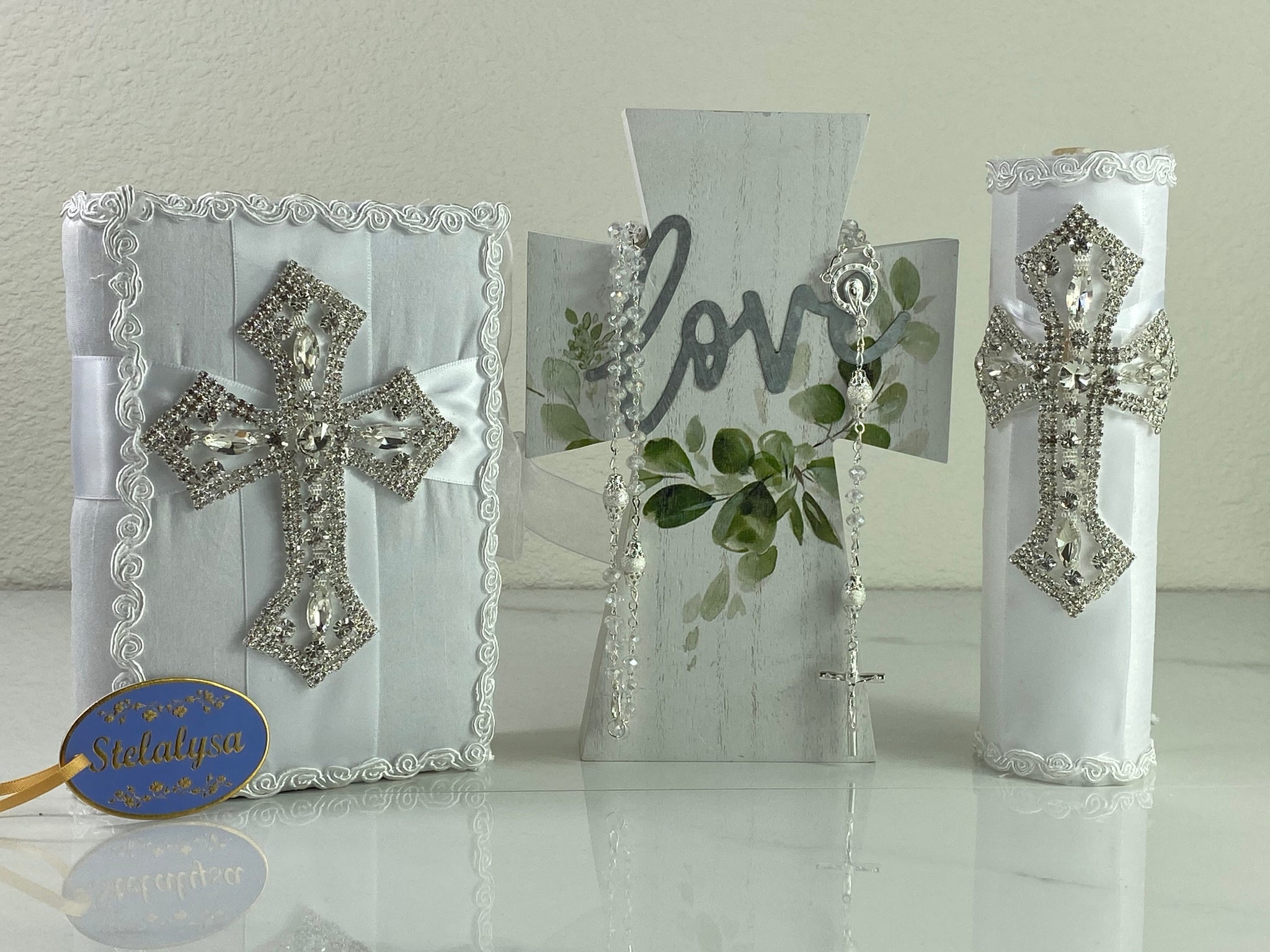 This white Bible Set - candle and bible is handmade and made using satin.  It is elegantly designed with lace and rhinestones.  Each piece has a beautiful huge cross.  The candle is an oval prism in shape.  An elegant rosary complements this set.  The rosary is 16.5 in. long and Bible is 6.5 in. by 4.5 in. and the candles approximately the same height.  The Bible includes the Old and New Testament in English. 