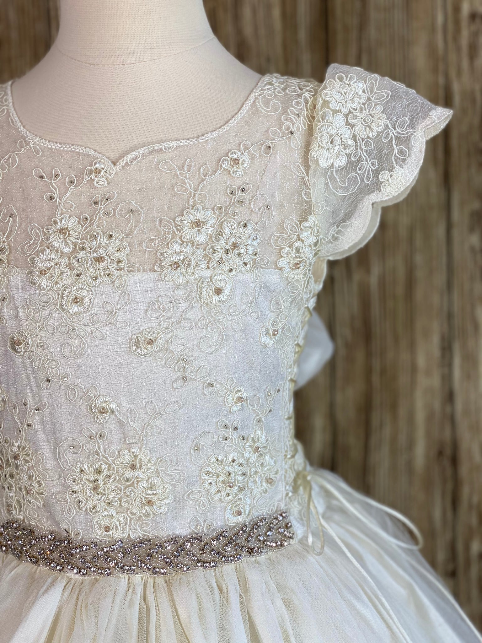 Ivory, size 10 Scalloped cap sleeve Ivory embroidered lace along illusion bodice and sleeve Elegant rhinestone band along lower bodice Gathered tulle skirt Corset closures on right and left underarms Ivory pearl button closure Ivory satin ribbon for large bow