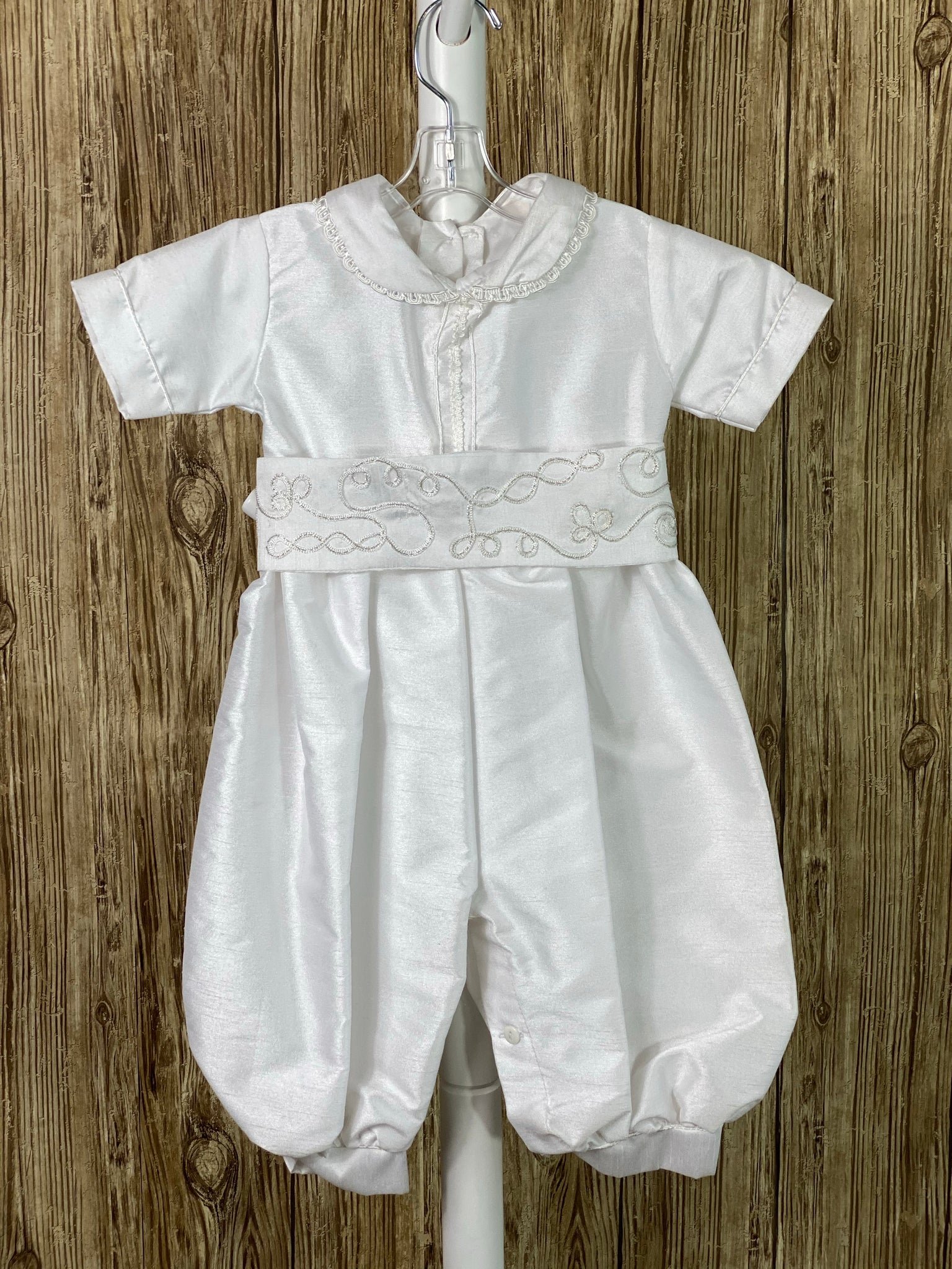 This a beautiful, one-of-a-kind boy’s baptism gown/set.  Lovely clothes for a precious child.  White, size 12M 4-piece set including beret, romper, belt, and mozzetta Buttoning on cuffs Collared with short sleeves Buttoning on back of romper and inside seam of legs Simple satin romper with very thin trim along cuffs and down center of bodice Braided trim swirled around belt and mozzetta Braided rope closure on mozzetta