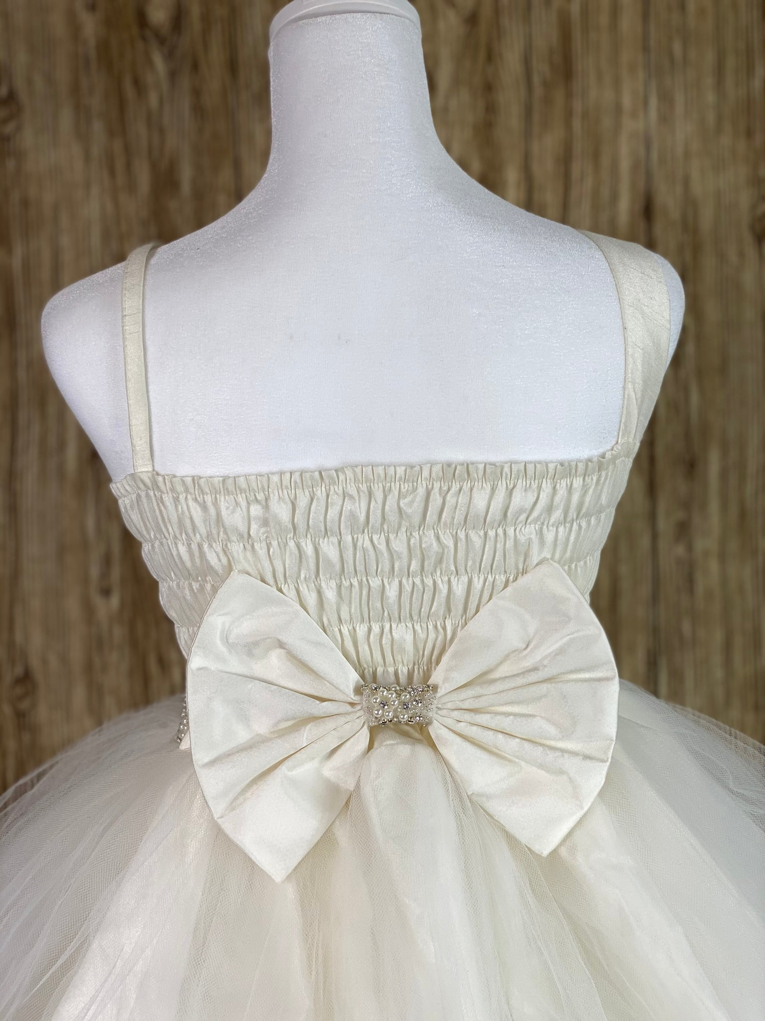 Ivory, size 12 Satin bodice with beaded lace overlay Flower on shoulder Rhinestone and pearl band along waist Gathered tulle skirt Shirred back Large satin bow in back
