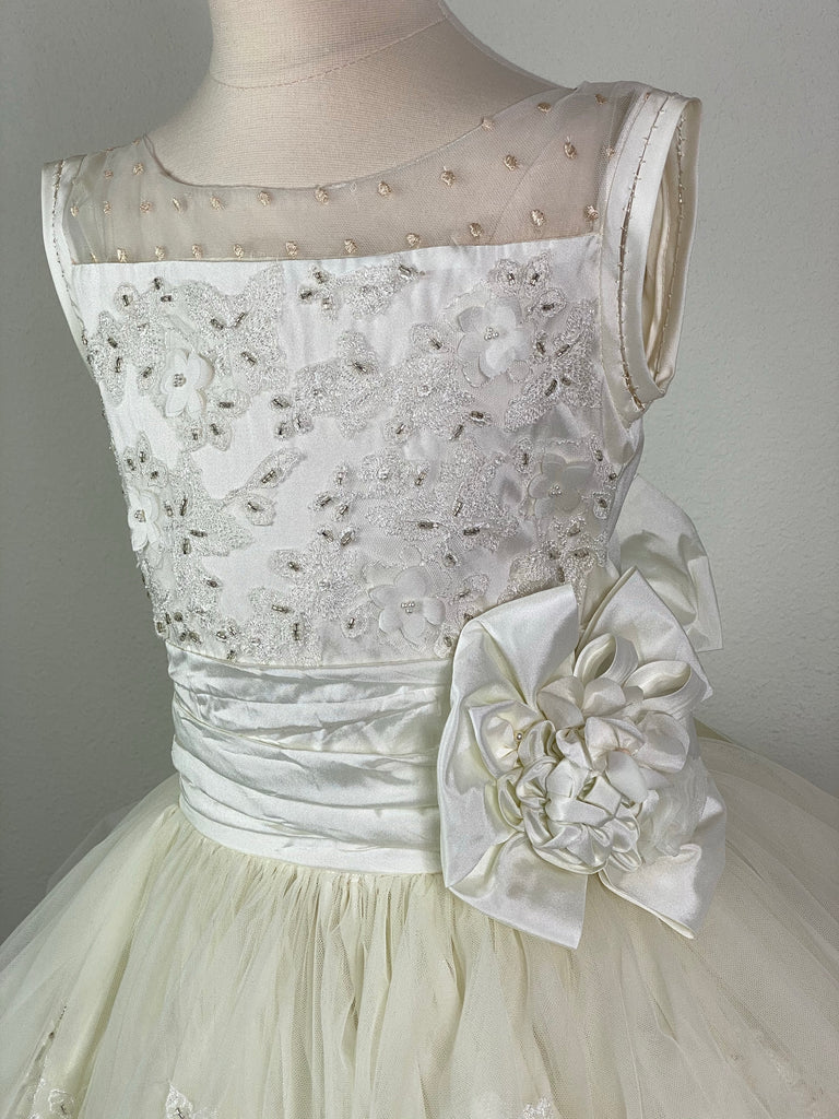 Beige dotted mesh and ivory embroidered satin illusion bodice Ivory ruched cummerbund with large flower Layered ivory tulle over ivory satin skirt Embroidered edging on all skirt layers Satin button closure Ivory satin ribbon for large bow Size 8 and 10