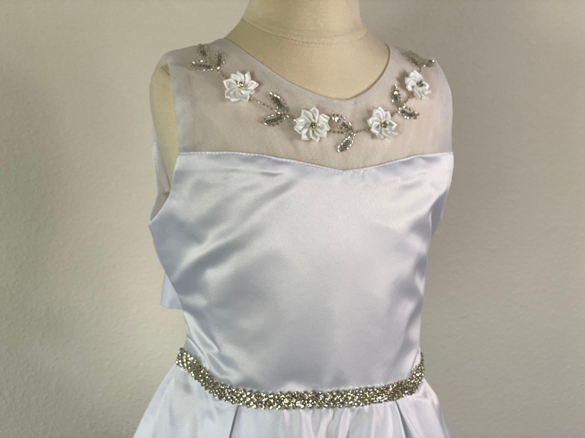 White, size 10 Satin and lace illusion bodice with flowers and beaded leaves Rhinestone belt Satin skirt Zipper Closure Satin ribbon for bow