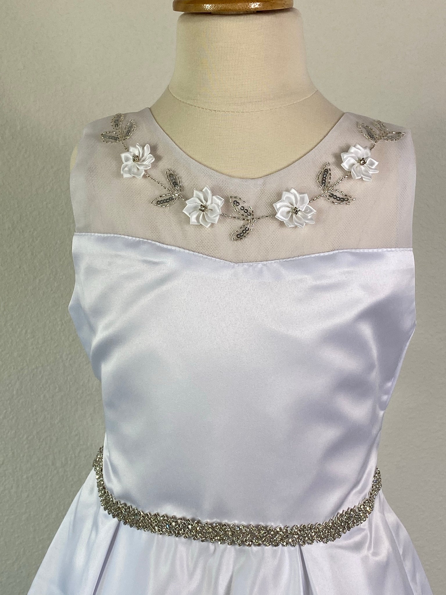 White, size 10 Satin and lace illusion bodice with flowers and beaded leaves Rhinestone belt Satin skirt Zipper Closure Satin ribbon for bow