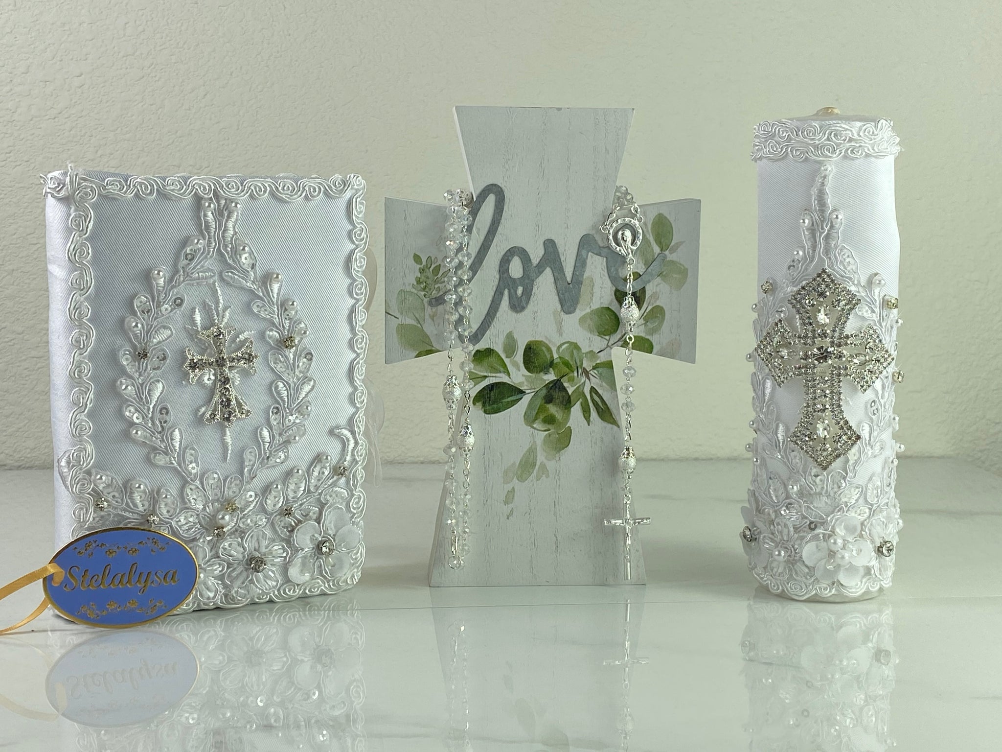 This white Bible Set - candle and bible is handmade and made using satin and lace.  It is elegantly designed with pearls, crystals, flowers in different pastel colors, and beads.  Each piece has a beautiful cross.  An elegant rosary complements this set.  The candle is cylinder in shape.  The rosary is 16.5 in. long and Bible is 6.5 in. by 4.5 in. and the candles approximately the same height.  The Bible includes the Old and New Testament in English. 