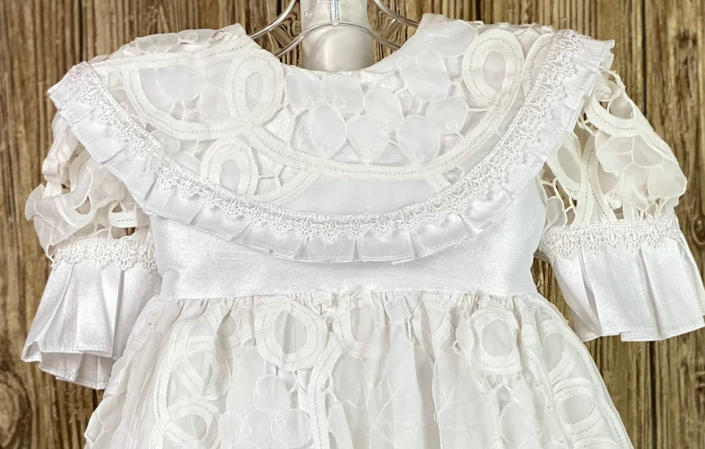 This a beautiful, one-of-a-kind baptism gown.  A lovely gown for a precious child.  White, size 12M Double layer dress Satin bodice with rounder lace collar Lace sleeves with pleated stain trim Lace skirting with pleated ribbon trim Second layer skirting of embroidered harlequin satin Button closure Satin bow in back Lace bonnet with pleated satin brim Mesh ribbon closure