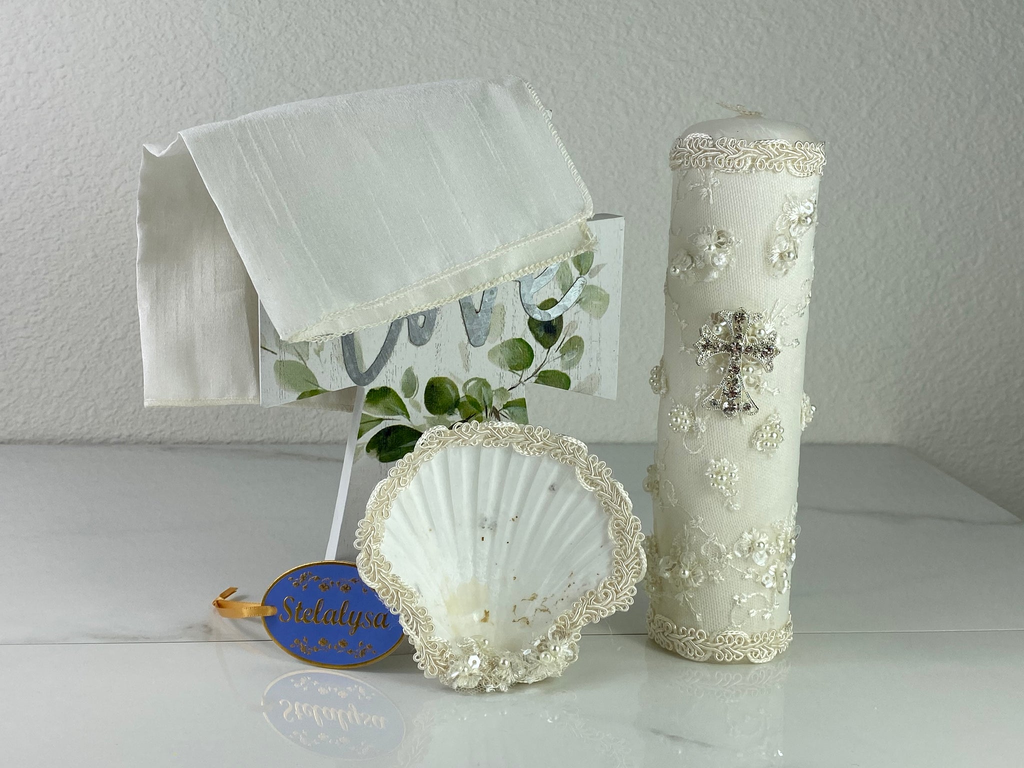 These one-of-a-kind Candle set is handmade and ivory in color.  This candle has a classic look.   It is uniquely decorated with a cross made of crystals, pearl clusters, and lace  making it a gorgeous keepsake.   This candle is cylinder in shape.  To match, the Shell is put together piece by piece to compliment the Candle and Handkerchief.  The Handkerchief is made of satin and embroidered lace to match the Shell and Candle beautifully.  