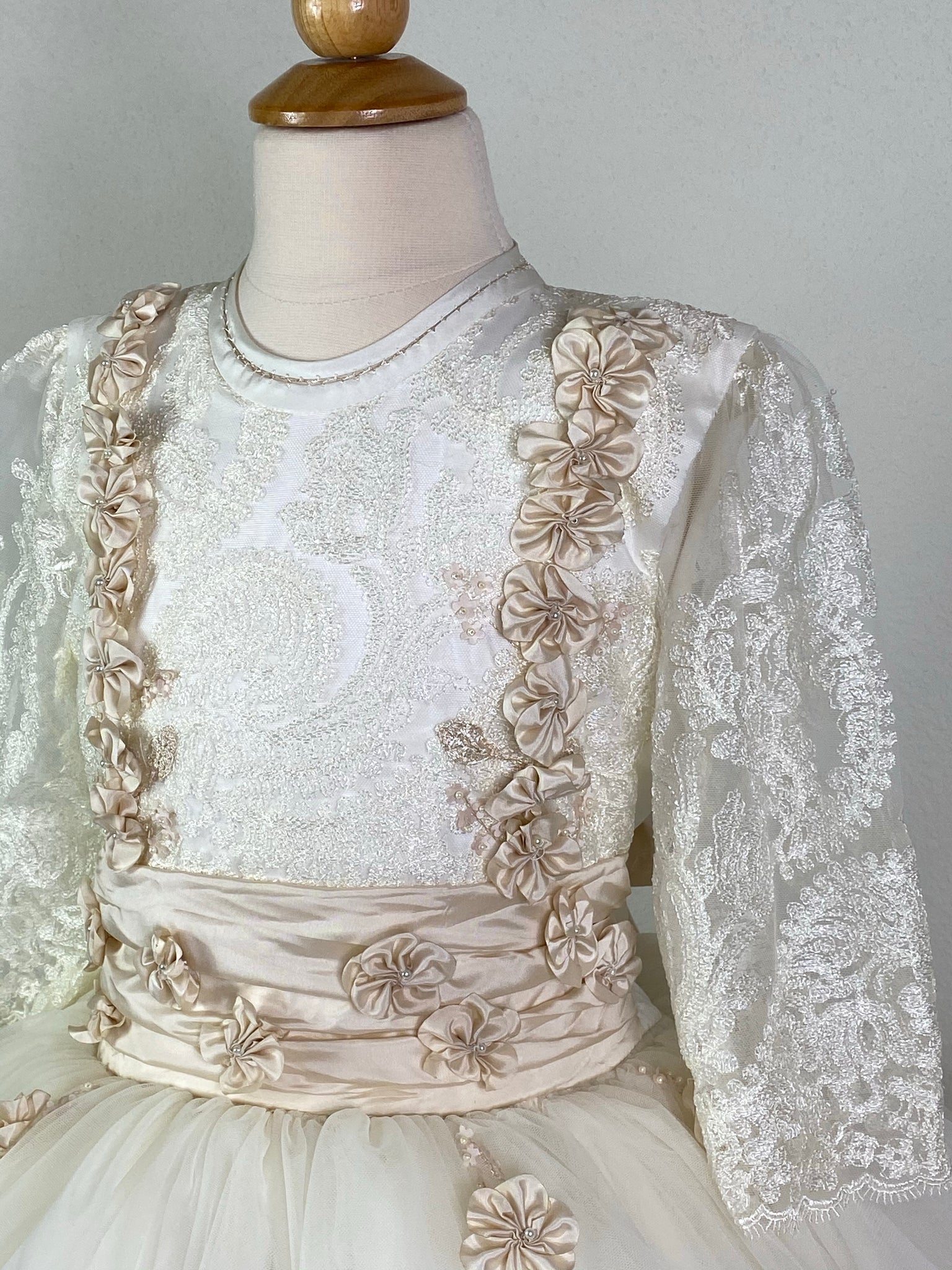 Ivory, size 10 3/4th ivory lace sleeve Hand stitched trim along neckline Embroidered lace bodice with floral stripes Small pearls in all flower detailing Champagne cummerbund with Champagne flowers within Layered tulle skirting with scattered Champagne flowers Pearl button closure Champagne satin ribbon for large bow