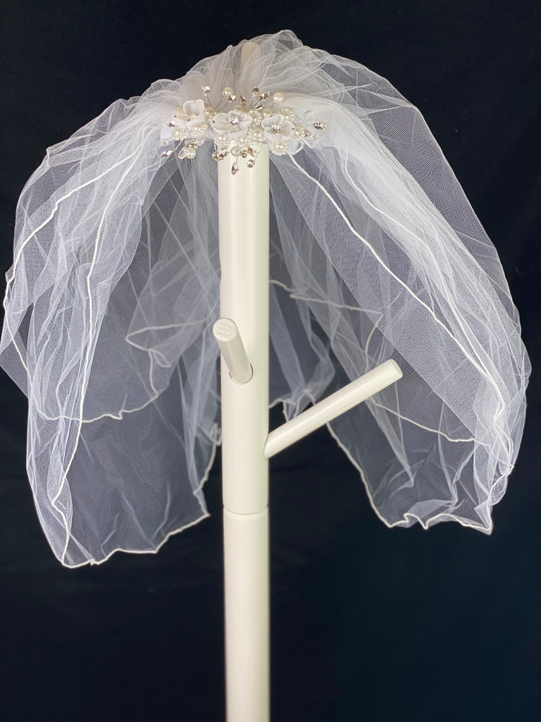 Veil - White Elegant First Communion Veil on Decorative Comb  Elegant soft 2 layer tulle veil with delicate hand stitched braided satin trim around the edge and handmade decorative comb with beautiful organza flowers through center with rhinestones on petals and centers. Stunning rhinestone leaves surrounding the flowers. Pearl flower clusters throughout comb.  This double layered veil reaches approximately 21" long. Veil has 2" long, 3" wide, comb to secure it in place. 