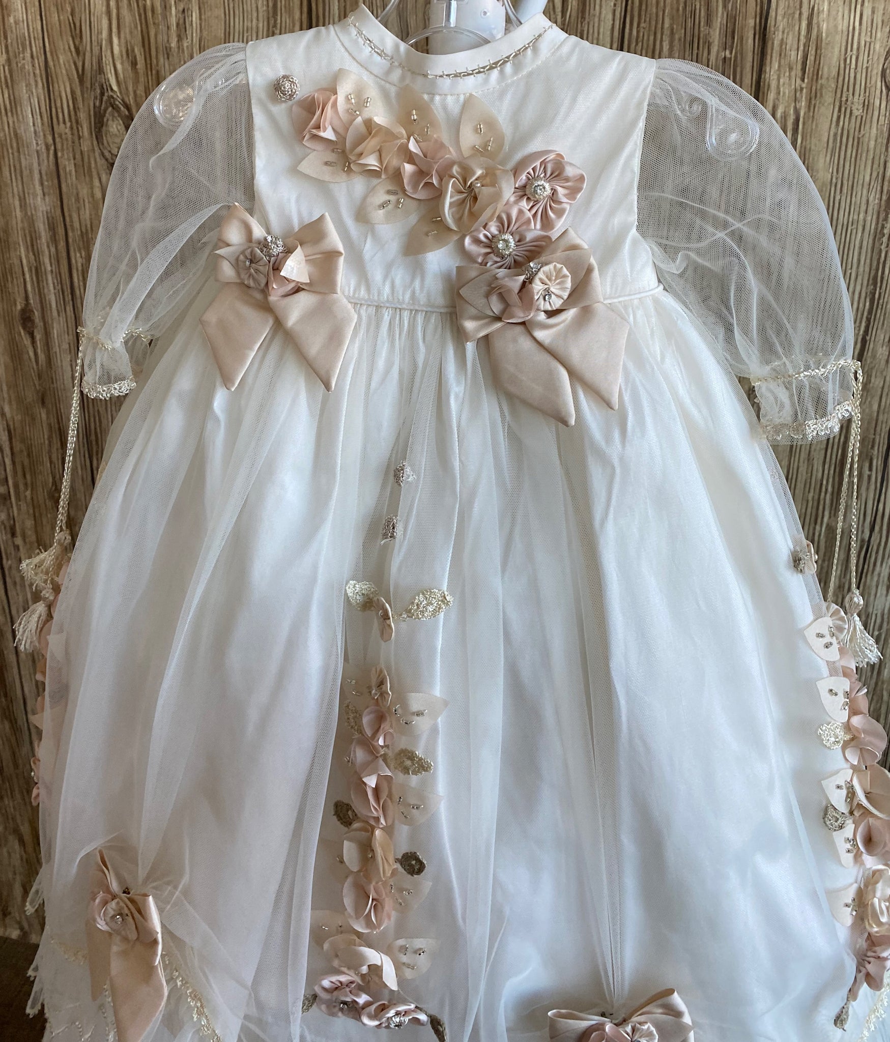 his a beautiful, one-of-a-kind baptism gown.  A lovely gown for a precious child.  Dress, Ivory, size 12M Satin bodice with dusty rose flower detailing Tulle half sleeve Large Champaign bows with flower center Dusty rose and Champaign flower pleats along tulle skirting Champaign bows on edge of skirting with tulle edge Slip  Satin bodice Layer one- thin pleated tulle overlay Layer two- tulle overlay with flowers Layer three- thick pleated tulle overlay