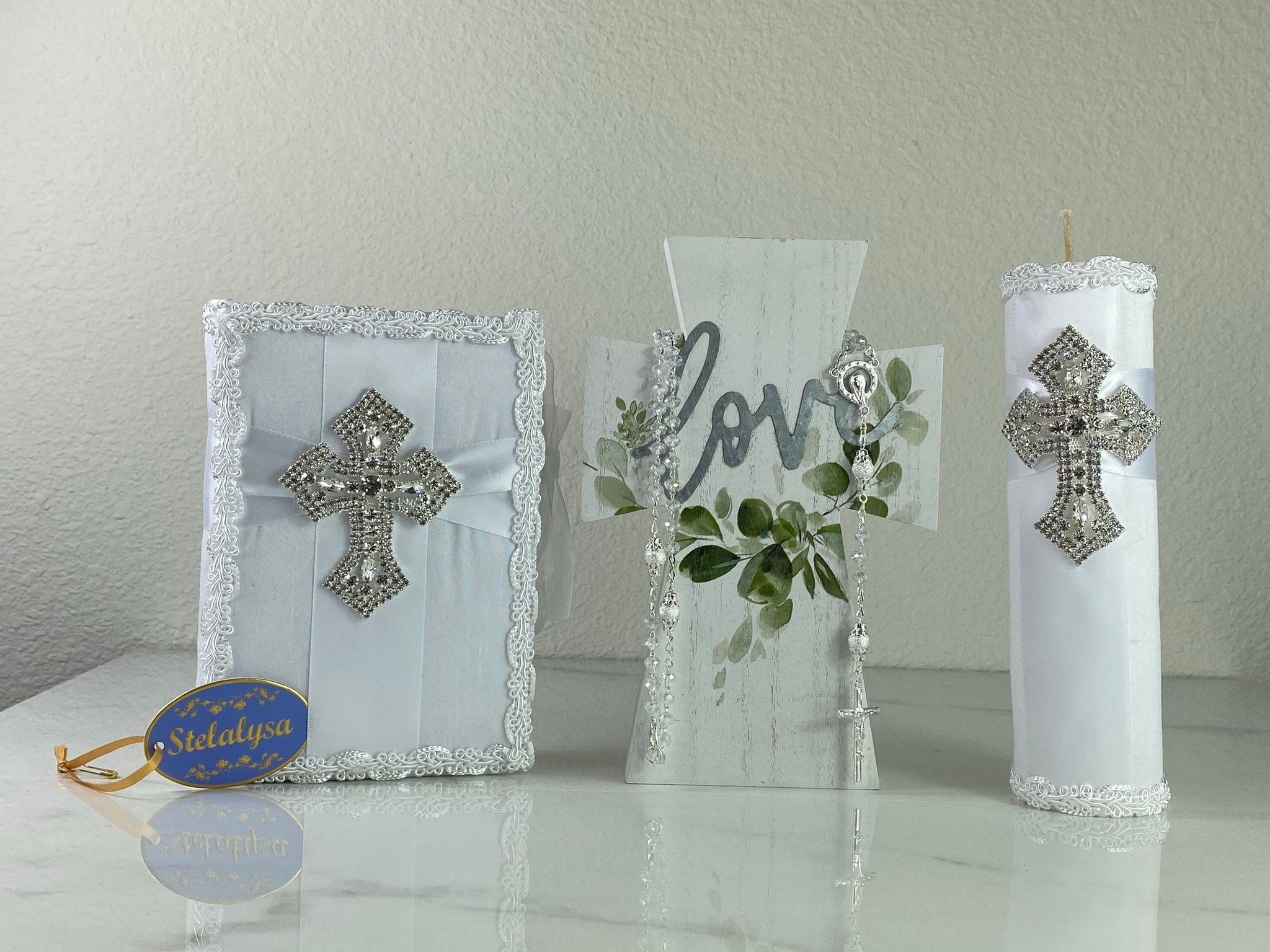 This white Bible Set - candle and bible is handmade and made using satin.  It is elegantly designed with lace and rhinestones.  Each piece has a beautiful cross.  The candle is cylinder in shape.  An elegant rosary complements this set.  The rosary is 16.5 in. long and Bible is 6.5 in. by 4.5 in. and the candles approximately the same height.  The Bible includes the Old and New Testament in English. 
