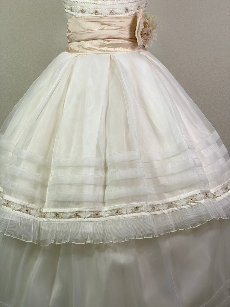 Ivory, size 12 Hand-stitched columned satin and flower bodice with crystals Extended scoop neckline Champagne cummerbund with ruffled bow Ivory tulle skirt with pleated trim and stripes along bottom Detachable skirt for long dress or short dress Satin covered button closure Champagne satin ribbon for large bow