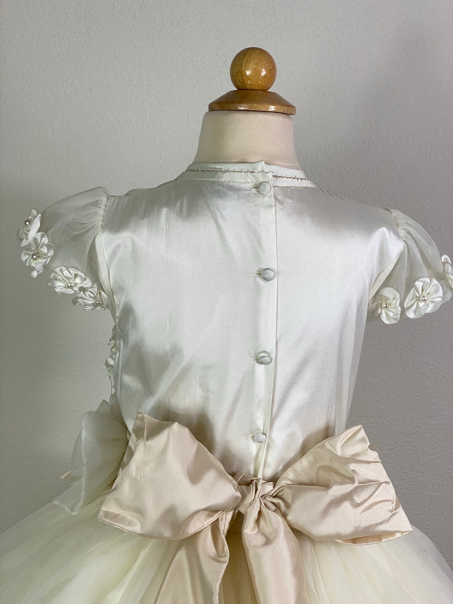 Ivory, size 10 Flowered mesh cap sleeve Satin and mesh illusion bodice Ivory flower detailing with pearl center on bodice and stripped-down tulle skirt Beige satin ruched cummerbund around waist with large flowered bow Ivory tulle overlay on satin skirt Satin covered button closure Beige ribbon for large bow