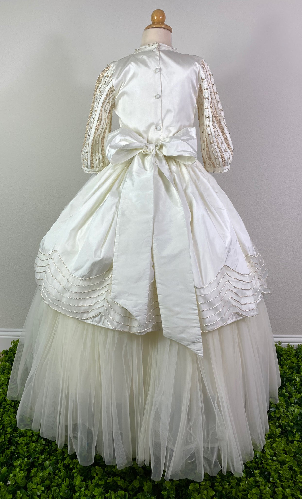 Ivory, size 10 Hand-stitched satin columned 3/4th sleeve Hand stitched satin columns with floral paneled bodice Ruched ivory cummerbund with large ivory ruffled bow Scalloped braided trim along edge of top skirt Floral detailing on under dress tulle Detachable dress for long dress or short dress Ivory Satin covered button closure Ivory Satin ribbon for large bow