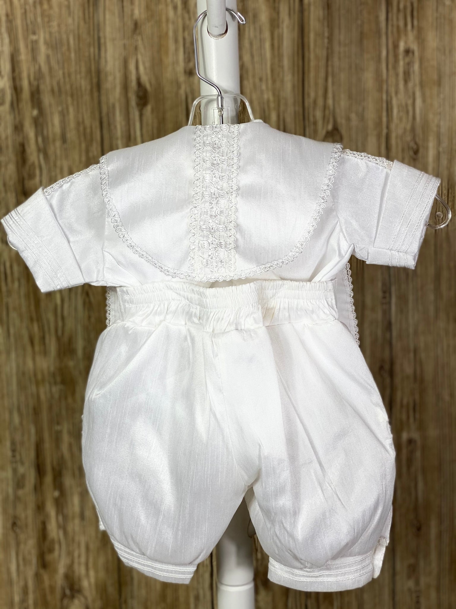 White, size 6M  4-piece set including Shirt, pants, stole, beret Collared shirt with short sleeves Buttoning on pant cuffs Elastic banding behind pants Button closure on back of shirt Thin trim striping pant legs, arm cuffs, stole, and cummerbund Crochet crosses on both sides of stole with rhinestone detailing Intricate lace ribbon down both sides of stole, beret, shirt bodice, and arms. Braided ribbon for stole closure