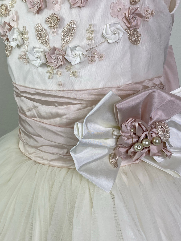 Ivory, size 10 Hand-stitched edging along arm holes and neckline Antique Rose and Ivory floral detailing with pearl center Antique Rose ruched cummerbund with pearl detailing in large bow Tulle skirt with antique rose satin trim Satin covered button closure Antique Rose ribboning for large bow Antique Rose satin trim