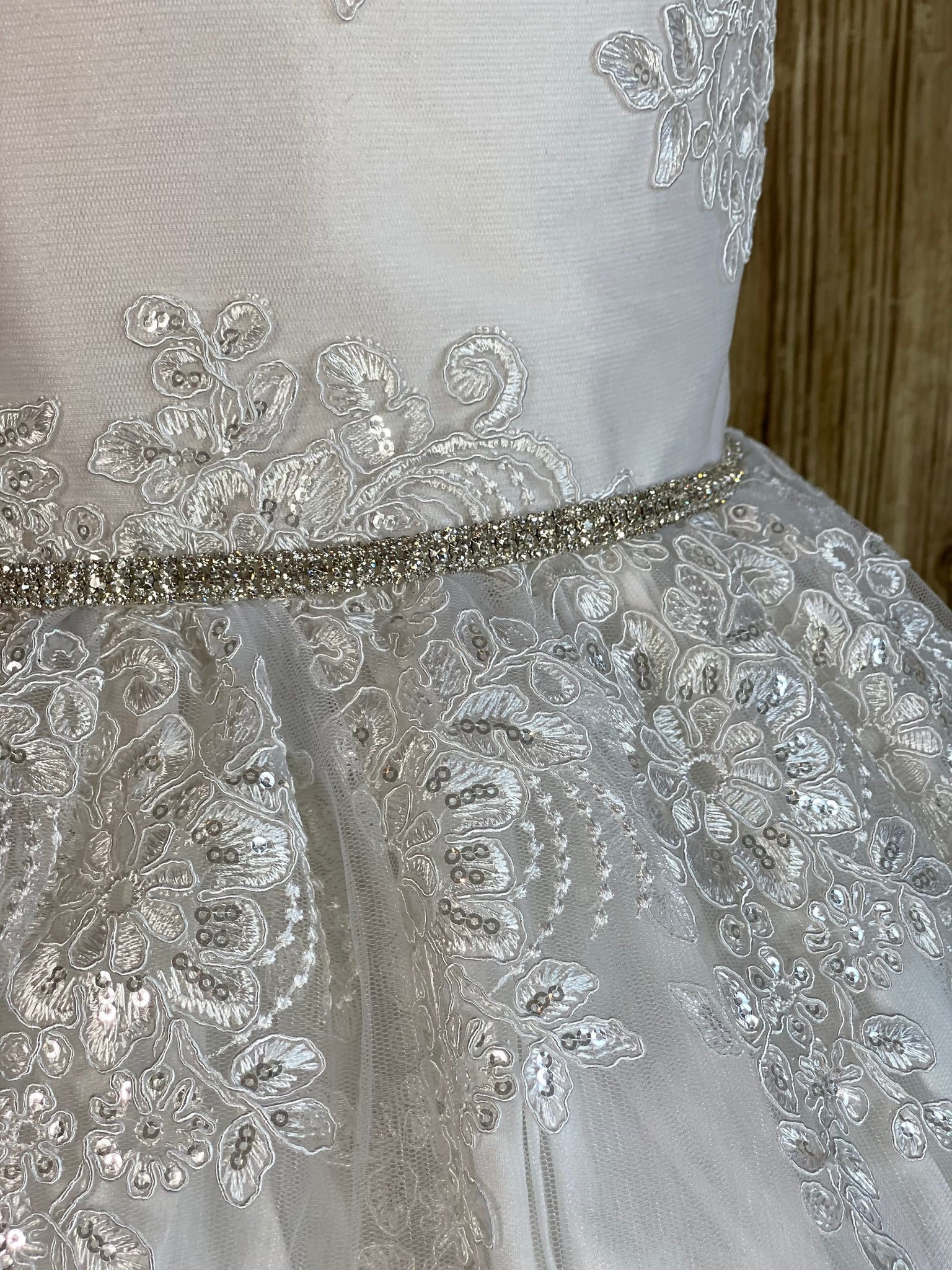 White, size 8 Lace cap sleeve Embroidered bodice with crystals throughout Rhinestone belt Satin skirt with embroidered tulle overlay and crystals Button closure Satin ribbon for bow