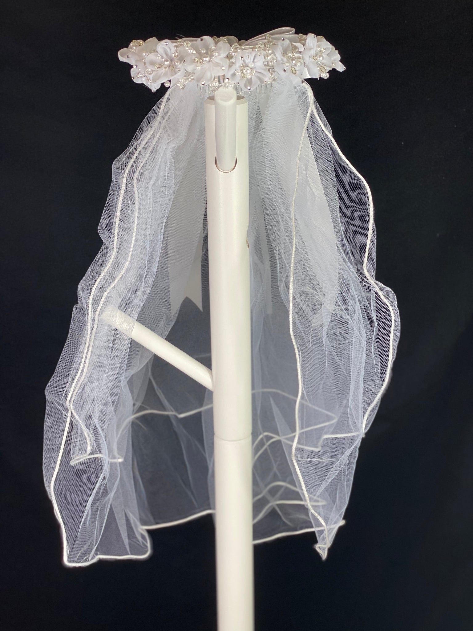 Elegant soft 2 layer tulle veil with delicate hand stitched braided satin trim around the edge and  Handmade flower halo crown with veil with large white satin bow on back. Organza flowers with sparkling rhinestone petals and pearl centers. Beautiful pearl leaves sticking out around flowers. This double layered veil reaches approximately 24" long, with a crown diameter of 6". Veil has 2" long, 3" wide, comb to secure it in place. 