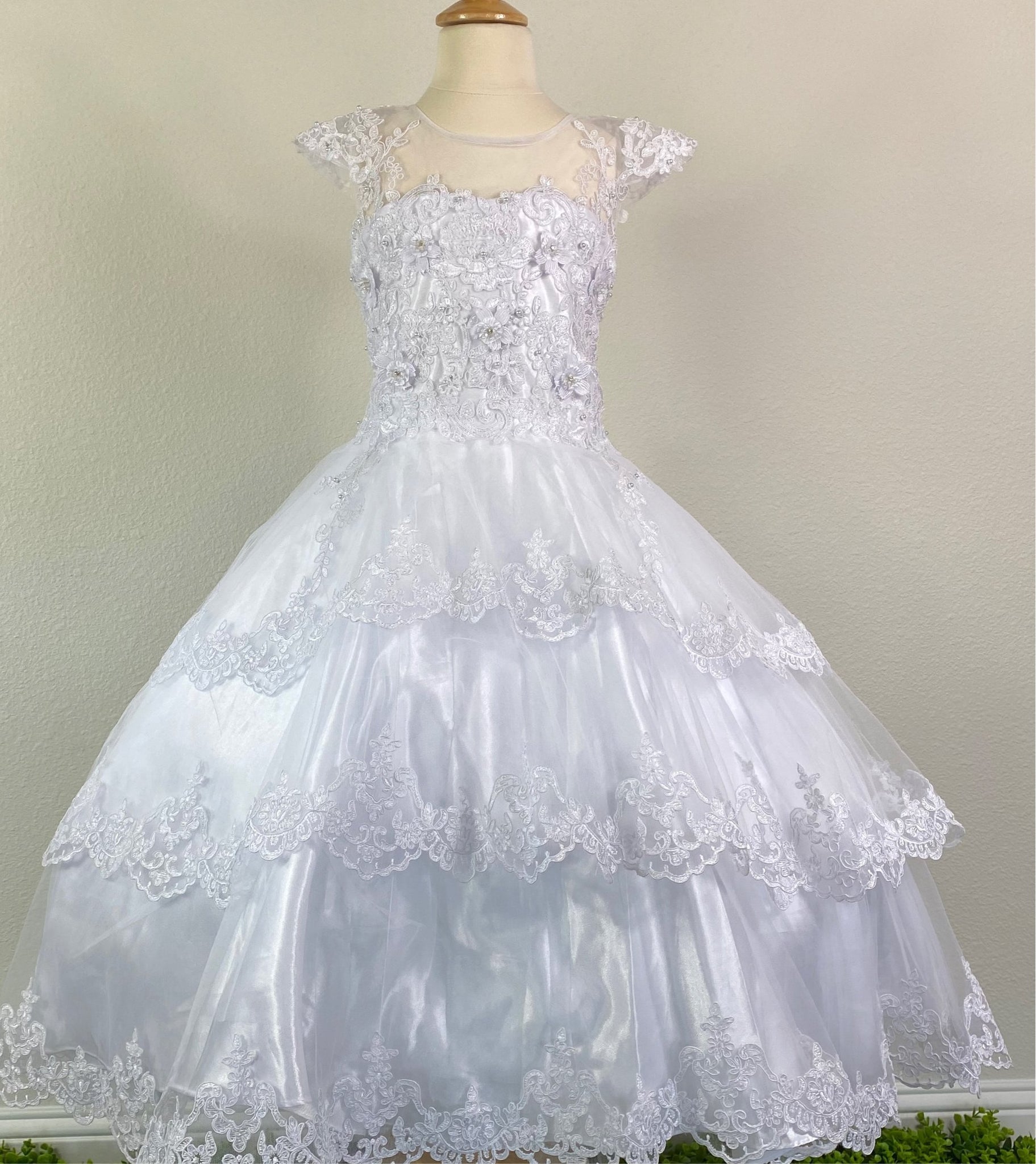 White, size 10 Satin trimmed cap sleeve with scoop neck Floral and lace illusion bodice with pearls and crystals Three-tiered embroidered lace trimmed skirt over satin underlay Zipper closure Satin ribbon for bow Short train