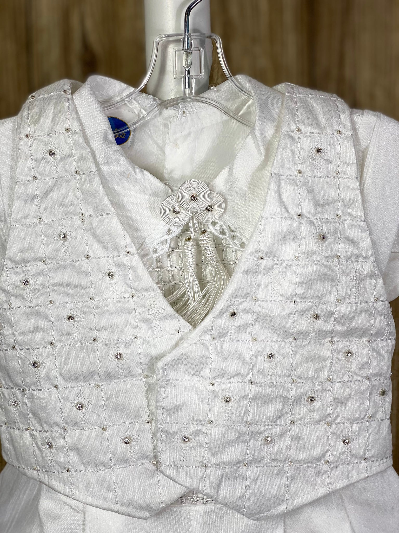 This a beautiful, one-of-a-kind boy’s baptism gown/set.  Lovely clothes for a precious child.  4- piece set including vest, shirt, pants, beret Satin, White pictures shown Grid pattern on vest with embroidered jeweled crosses in checkered pattern Grid pattern on pant legs, cummerbund, shirt bodice, and arm cuffs Intricate trim around cuffs and collar Thin lines around beret trim Tassel pin with 3 rhinestone centered circles