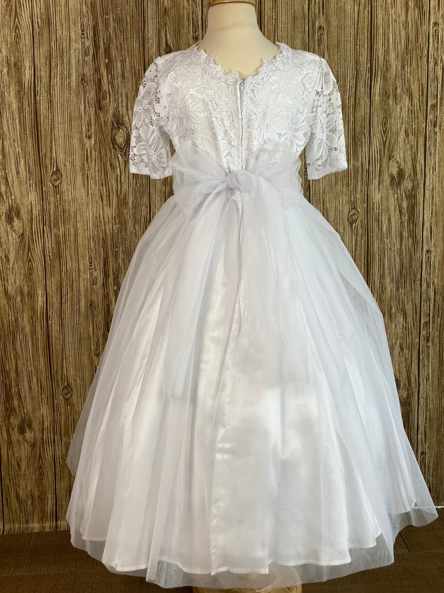 Fall in love with this First Holy Communion dress.  She will feel and look like a princess on her special event.   Lace quarter sleeve Scoop neck with floral trim Lace over satin bodice Floral belt Tulle over satin skirt Tulle ribbon for bow Zipper closure