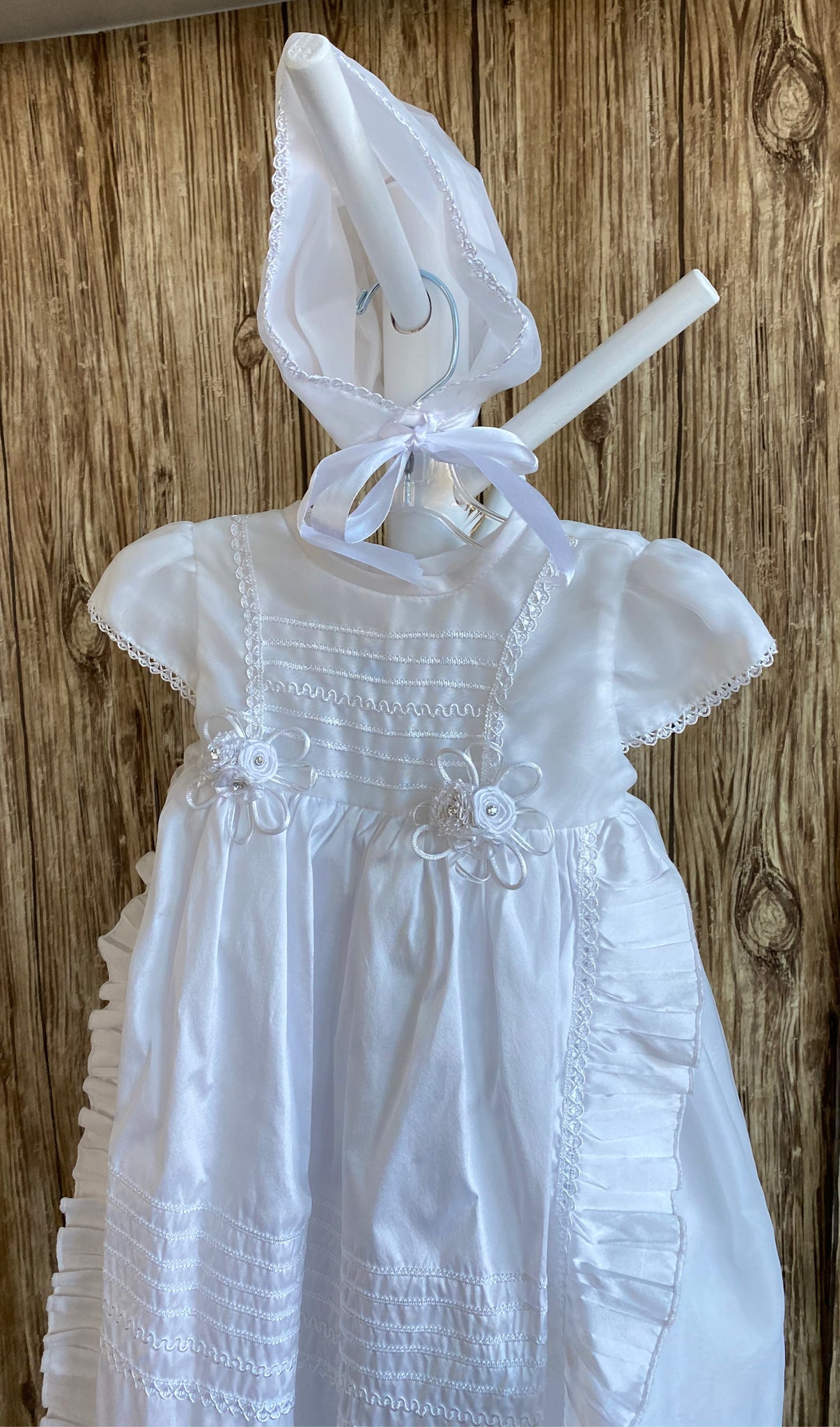 This a beautiful, one-of-a-kind baptism gown.  A lovely gown for a precious child.  White, size 12M Cropped satin bodice Embroidered detailing on bodice Two flowered bouquets on edging of bodice Satin cap sleeve with hand stitching along edge Long layered skirting Embroidered striping detailing on top layer of skirt Ruffled edge along skirt layers Satin bonnet with hand stitched edging Ribbon closure to tie around the head