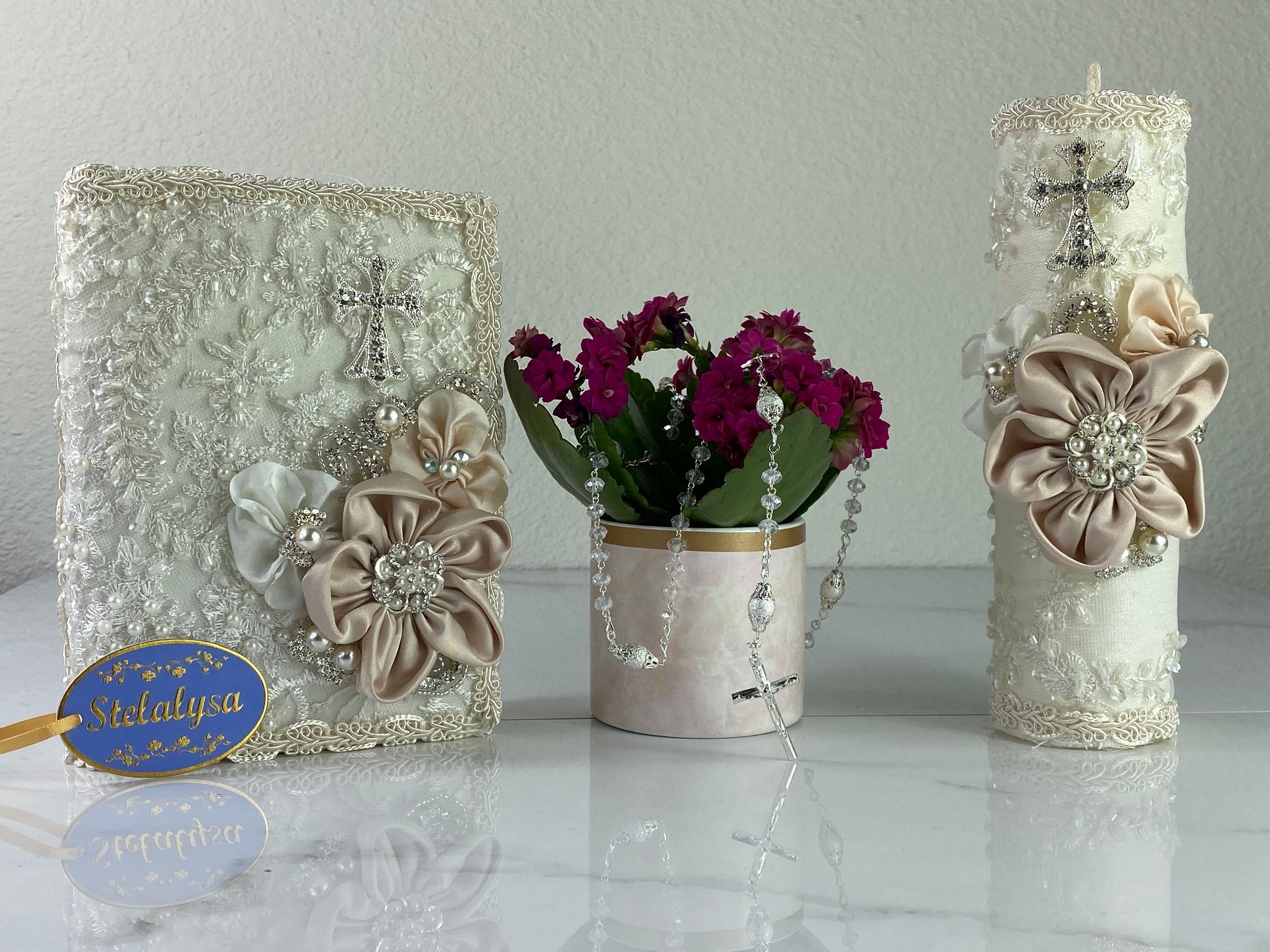 This ivory Bible Set - candle and bible is handmade and made using satin and lace.  It is elegantly designed with pearls, crystals, flowers in different pastel colors, and beads.  Each piece has a beautifully placed cross.  An elegant rosary complements this set.  The candle is cylinder in shape.  The rosary is 16.5 in. long and Bible is 6.5 in. by 4.5 in. and the candles approximately the same height.  The Bible includes the Old and New Testament in English. 