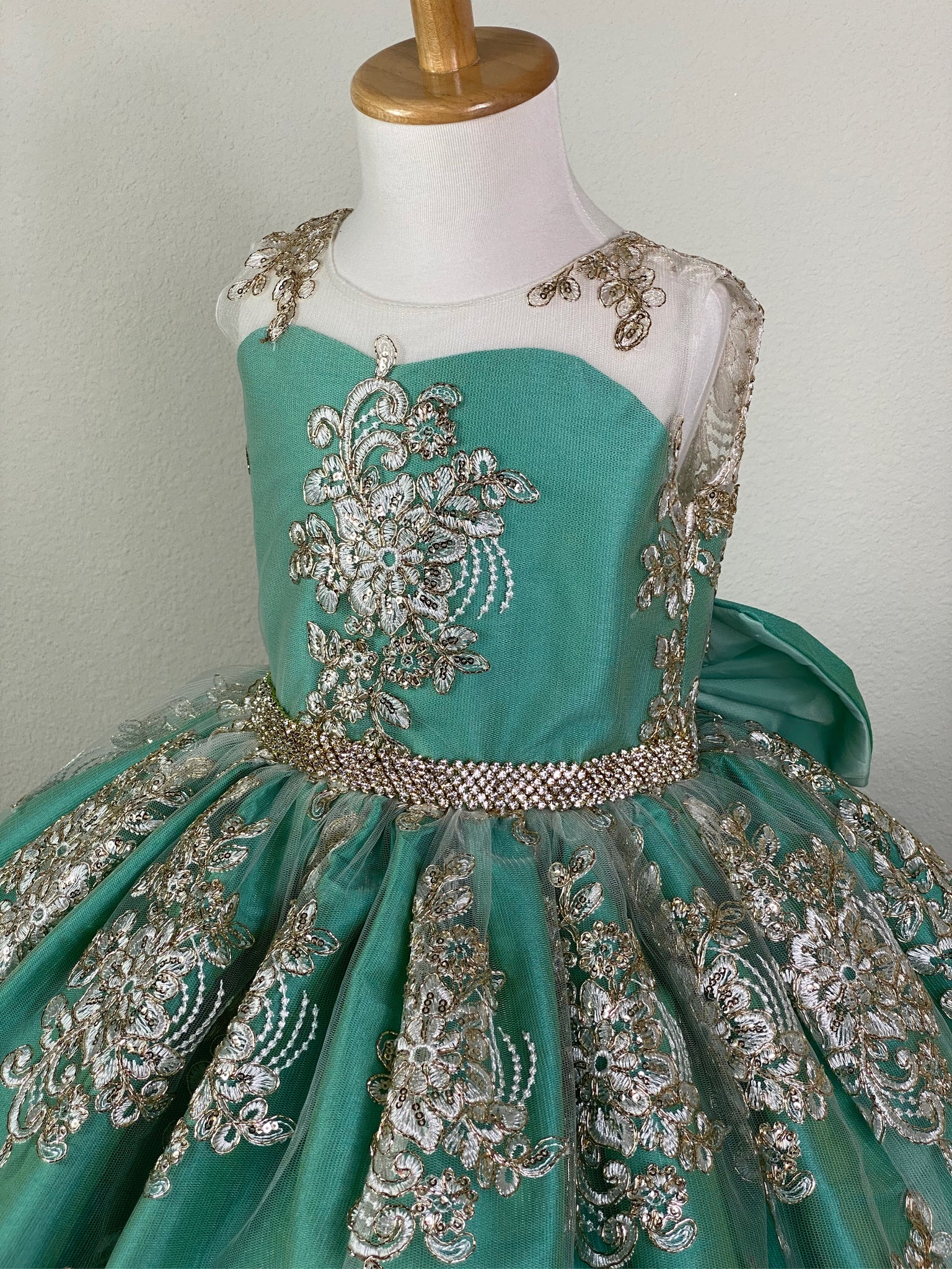 Menta Green, size 4 illusion bodice with embroidered white appliques on tulle Embellished rhinestone band along lower bodice Menta blue satin skirting with embroidered white appliques on tulle overlay Open back with button closure Large menta blue satin bow Dress pictured with a petticoat Petticoat not included  Choose from a tulle, cloth, or wire for best look