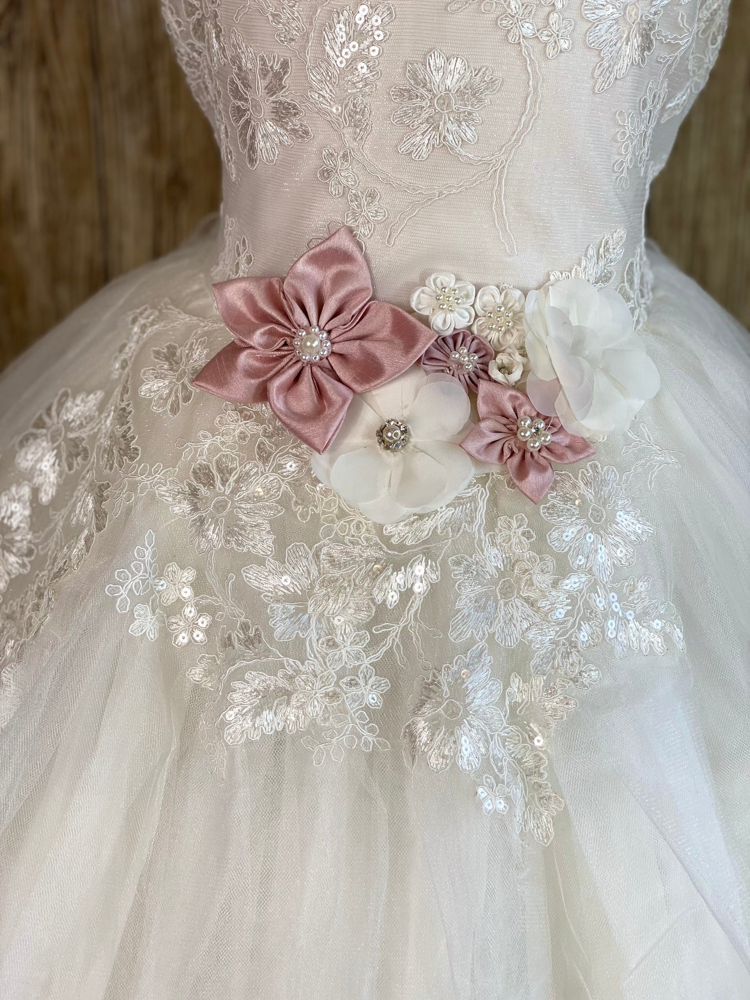 White, size 10 Scoop neck Floral lace bodice Embroidered floral lace detailing going diagonal on skirt Pearl flowers around lower bodice (mauve and white in color) Keyhole back with button closures Big satin bow on back