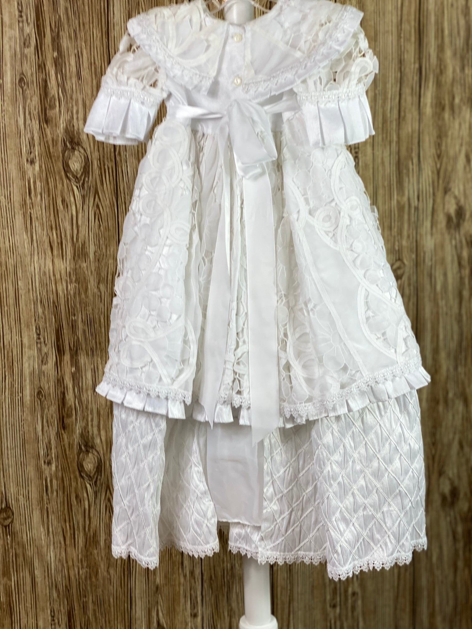 This a beautiful, one-of-a-kind baptism gown.  A lovely gown for a precious child.  White, size 12M Double layer dress Satin bodice with rounder lace collar Lace sleeves with pleated stain trim Lace skirting with pleated ribbon trim Second layer skirting of embroidered harlequin satin Button closure Satin bow in back Lace bonnet with pleated satin brim Mesh ribbon closure