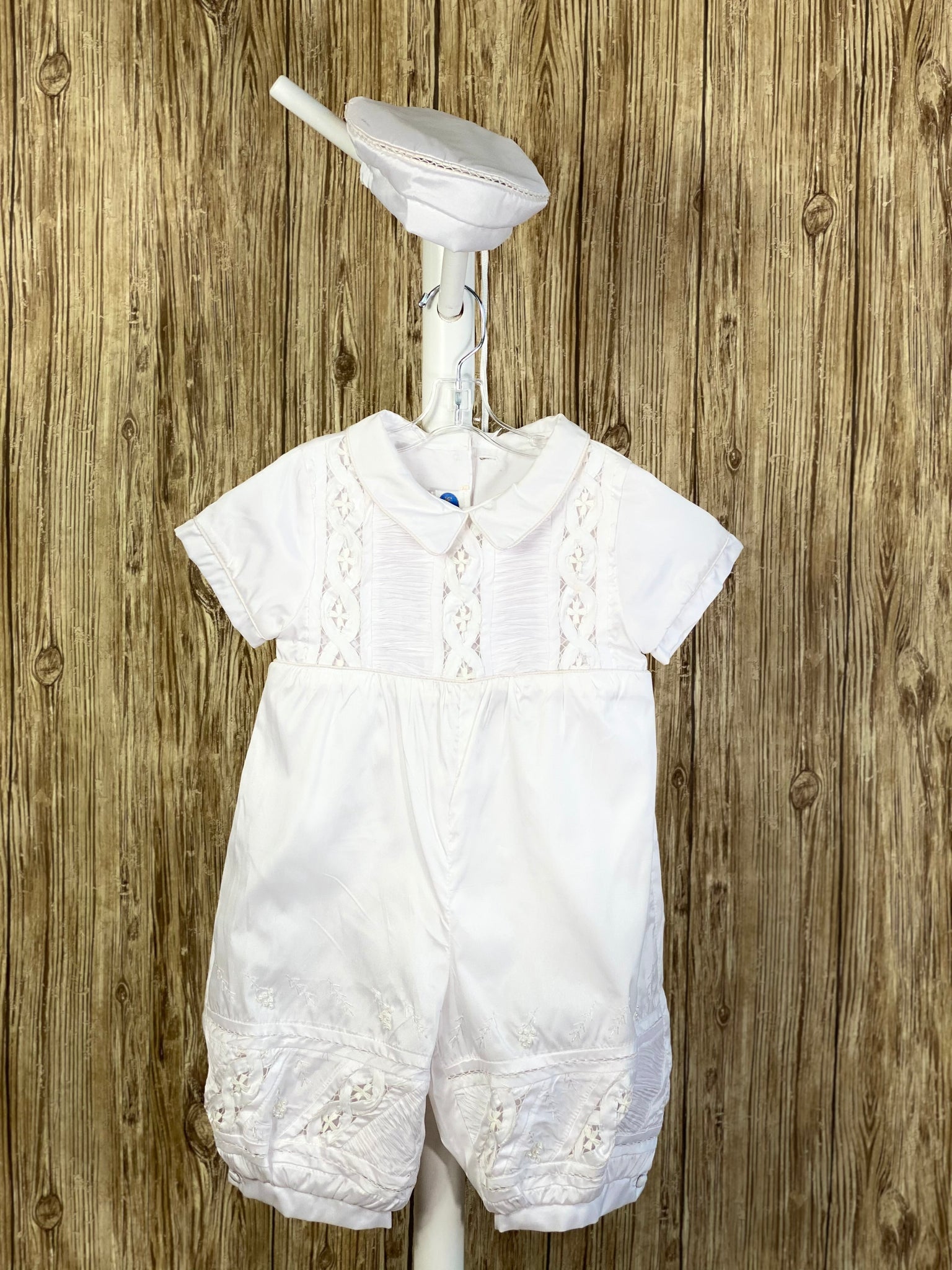 This a beautiful, one-of-a-kind boy’s baptism gown/set.  Lovely clothes for a precious child.  White, size 12M 2-piece set including romper and belt Buttoning on cuffs Collared with short sleeves Buttoning on back of romper Pleated columns on bodice and legs of romper Crochet cross lace columns on bodice and legs of romper Hand-stitched trim around legs of romper Hand-stitched leaf designs on legs of romper with pearl detailing inside Thin pin-striping on belt